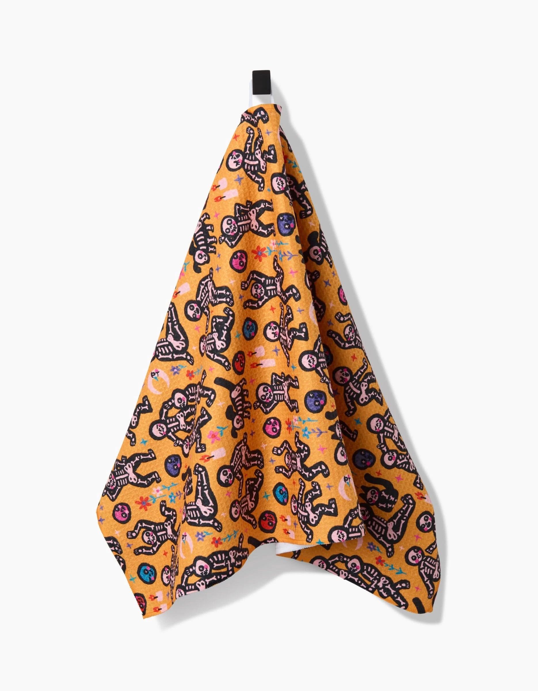 The So Lazo After Party tea towel, made from recycled materials, features a quick-drying yellow fabric with playful skeletons and colorful skulls, hanging by a black loop against a plain white background.