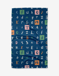 The Amy MacCready Alphabet blanket is navy blue with a playful mix of white, orange, green, and pink letters—some in colored squares. Made with recycled materials for a cozy, sustainable touch.
