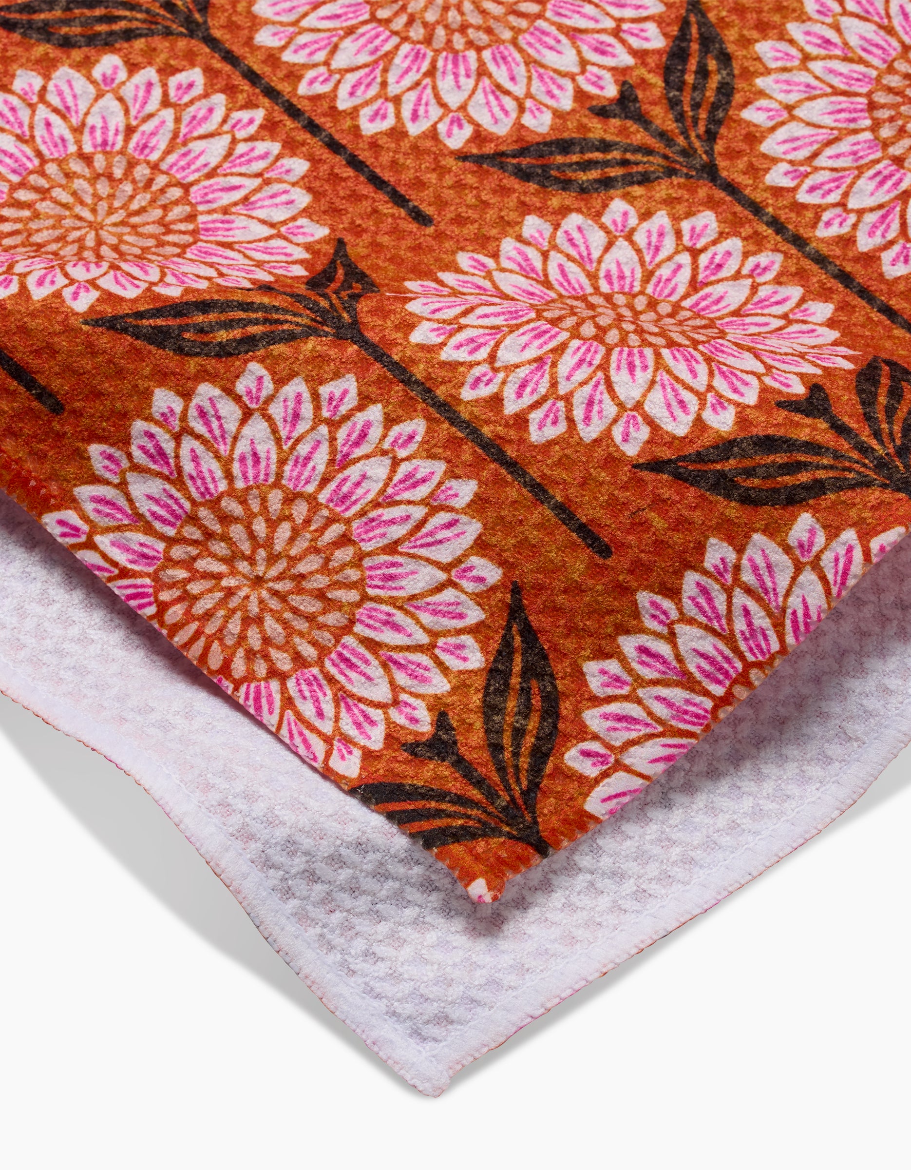 The Amber tea towel by Amy MacCready features an orange top with large pink and white floral designs, dark brown stems and leaves, a textured white underside, and is crafted from ultra-absorbent recycled materials.