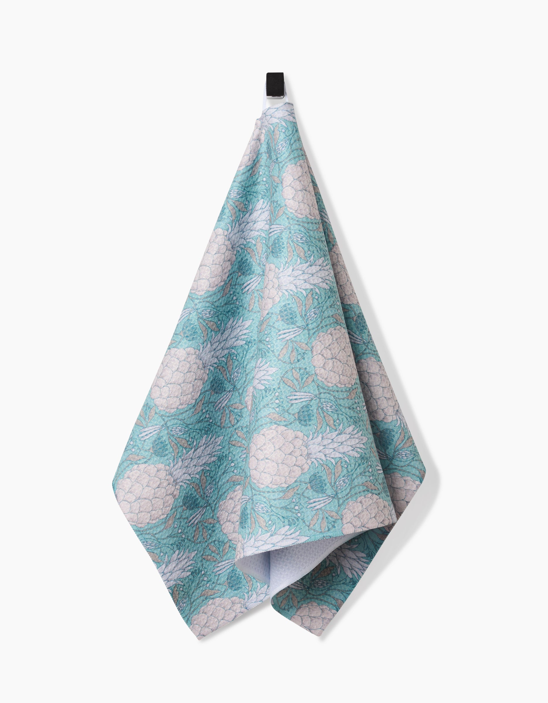 An Andre tea towel by Amy MacCready, crafted from Geoweave fabric, features a turquoise and white pineapple and leaf pattern. It hangs on a black hook against a white background.