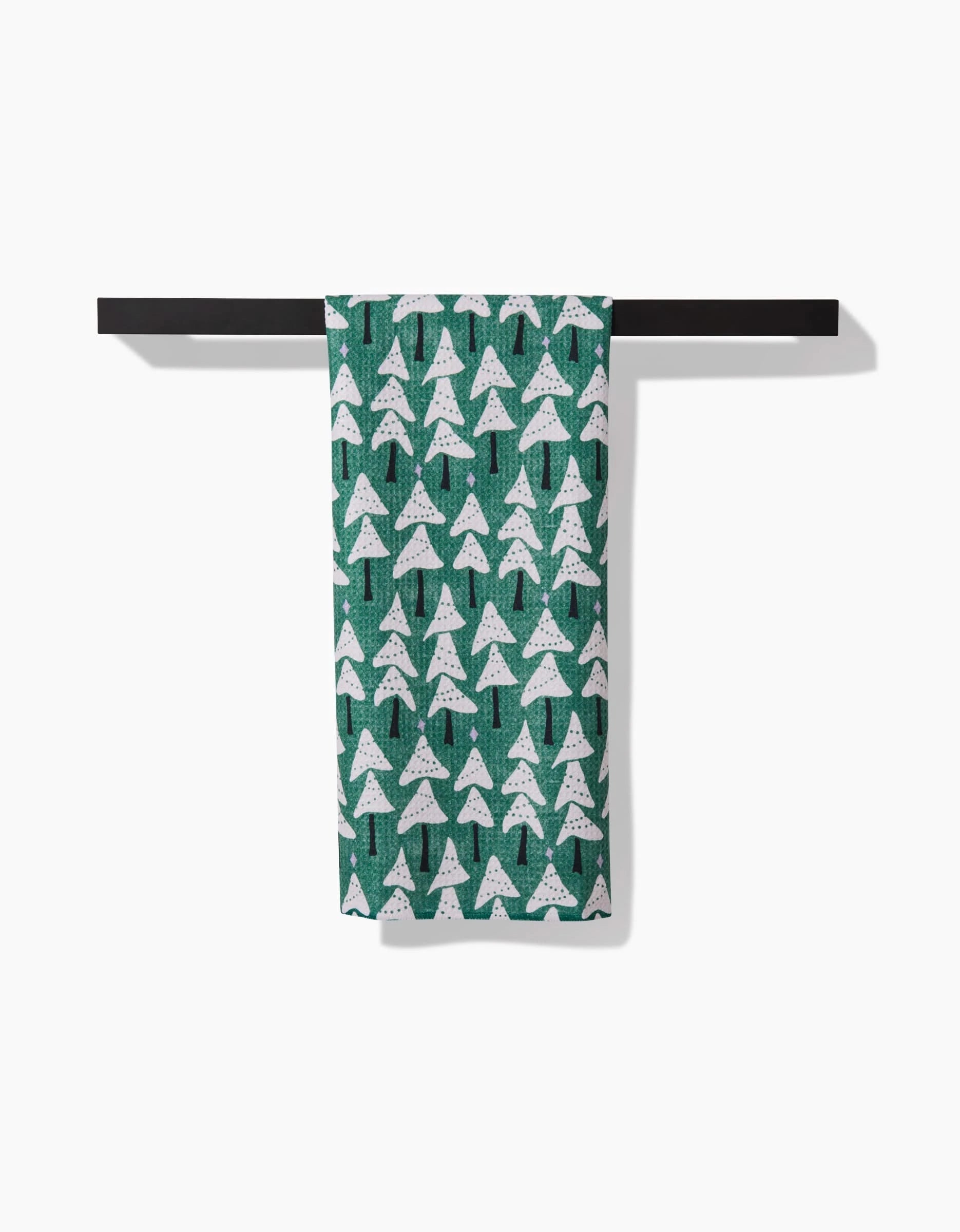 The Angelina kitchen towel by Amy MacCready, made from recycled material and featuring white pine trees, hangs neatly over a black towel bar against a white background.