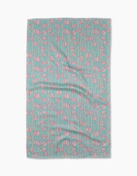 The Aqua Poppy Pods tea towel by Katie OShea is rectangular, crafted from recycled materials, and features pink and white abstract flowers with green stems on a light blue background. The slightly wrinkled fabric lies flat against a white surface.