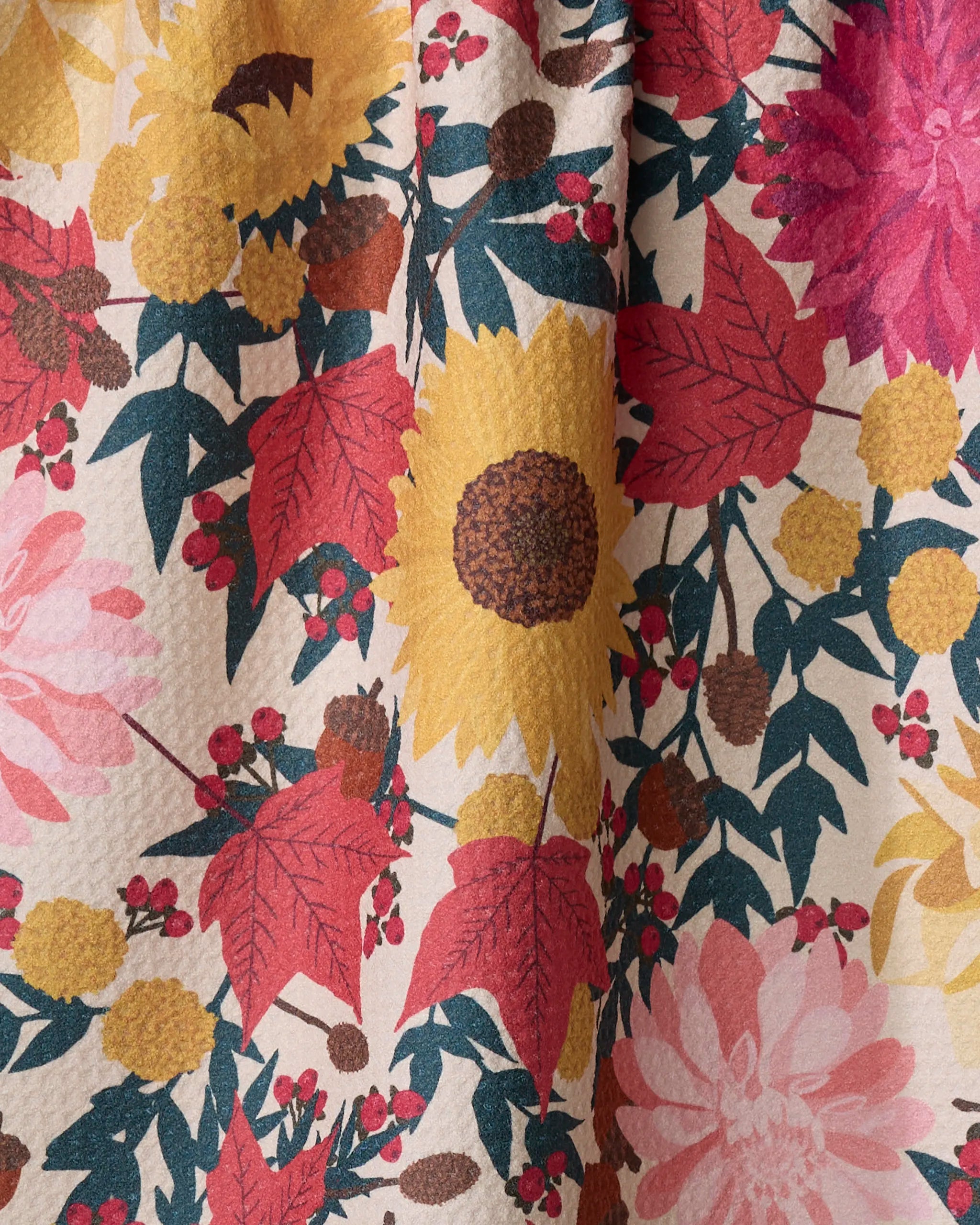 A close-up of the Rebecca Bobko "Autumn Blooms" eco-friendly kitchen towel, showcasing a vibrant floral pattern with yellow sunflowers, pink and red flowers, green leaves, and red berries on a cream background.