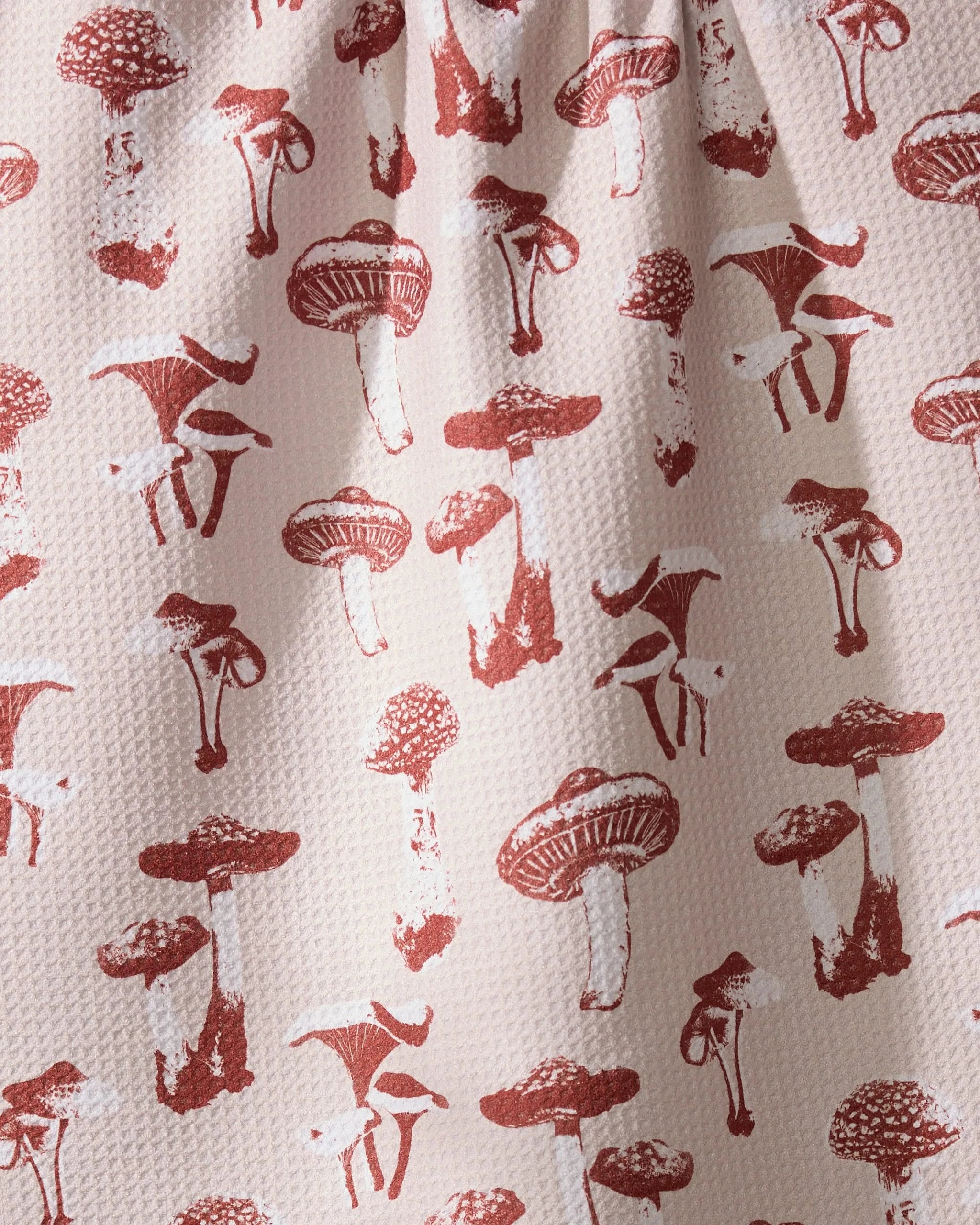 The Geometry Autumn Mushrooms tea towel features red mushroom illustrations on a textured white surface and is made from recycled materials.