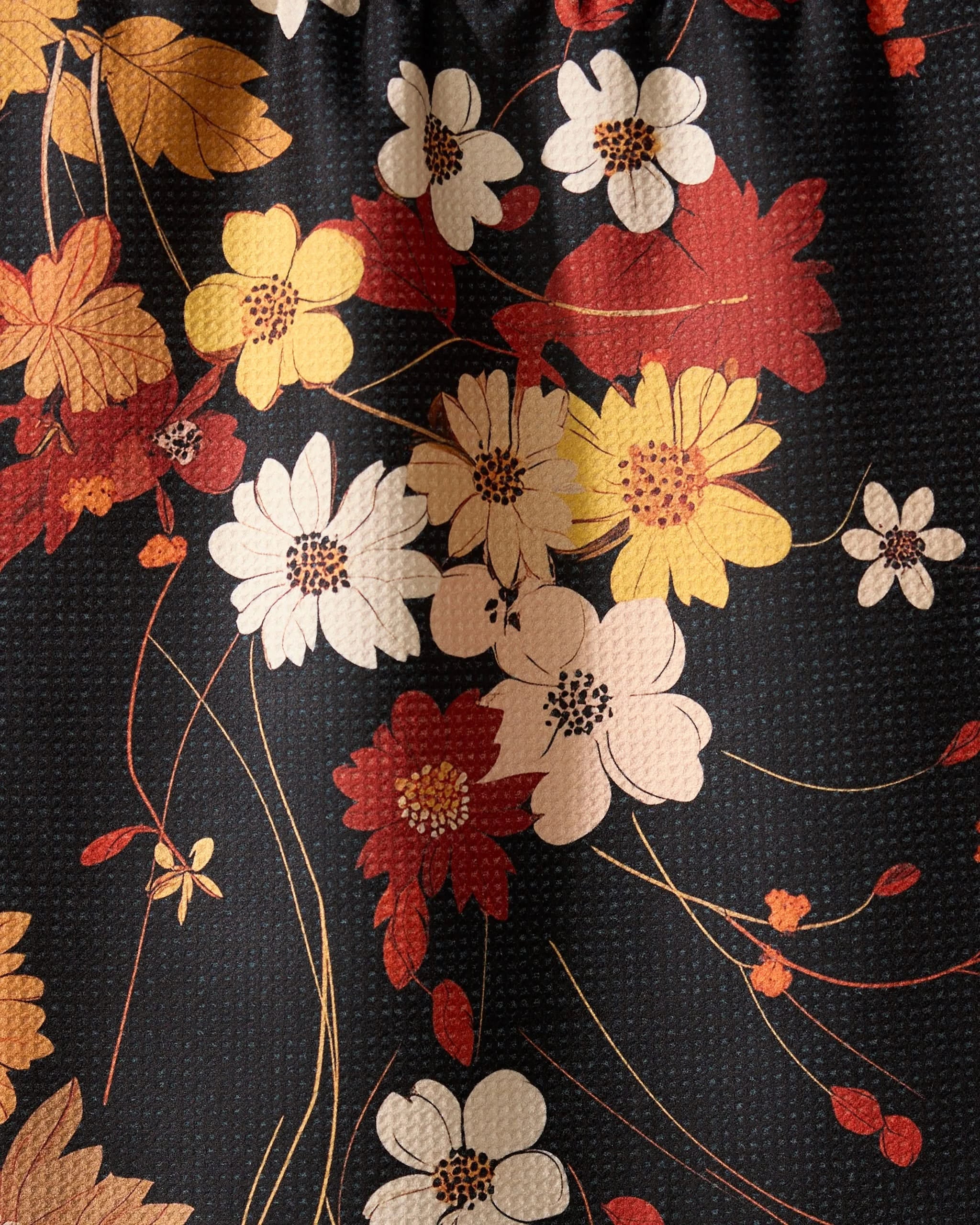 A close-up of the Geometry Autumn Whispers absorbent dish towel, showcasing its textured surface and a floral pattern with white, yellow, and red flowers plus green stems on a dark background.