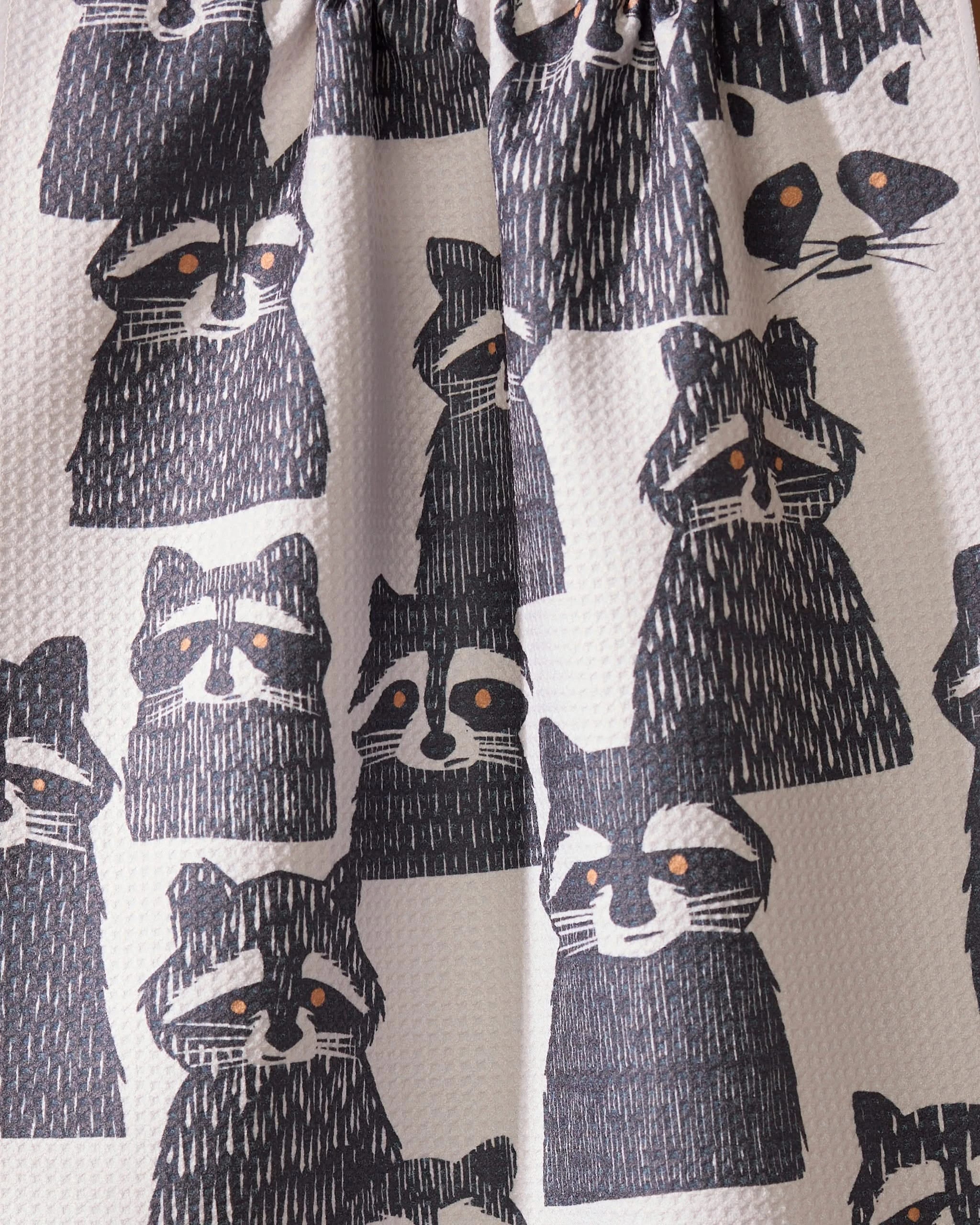 Banditbunch by Geometry features a playful pattern of black and white raccoon illustrations with orange eyes on a light background—ideal for adding a charming touch to your kitchen tea towels.