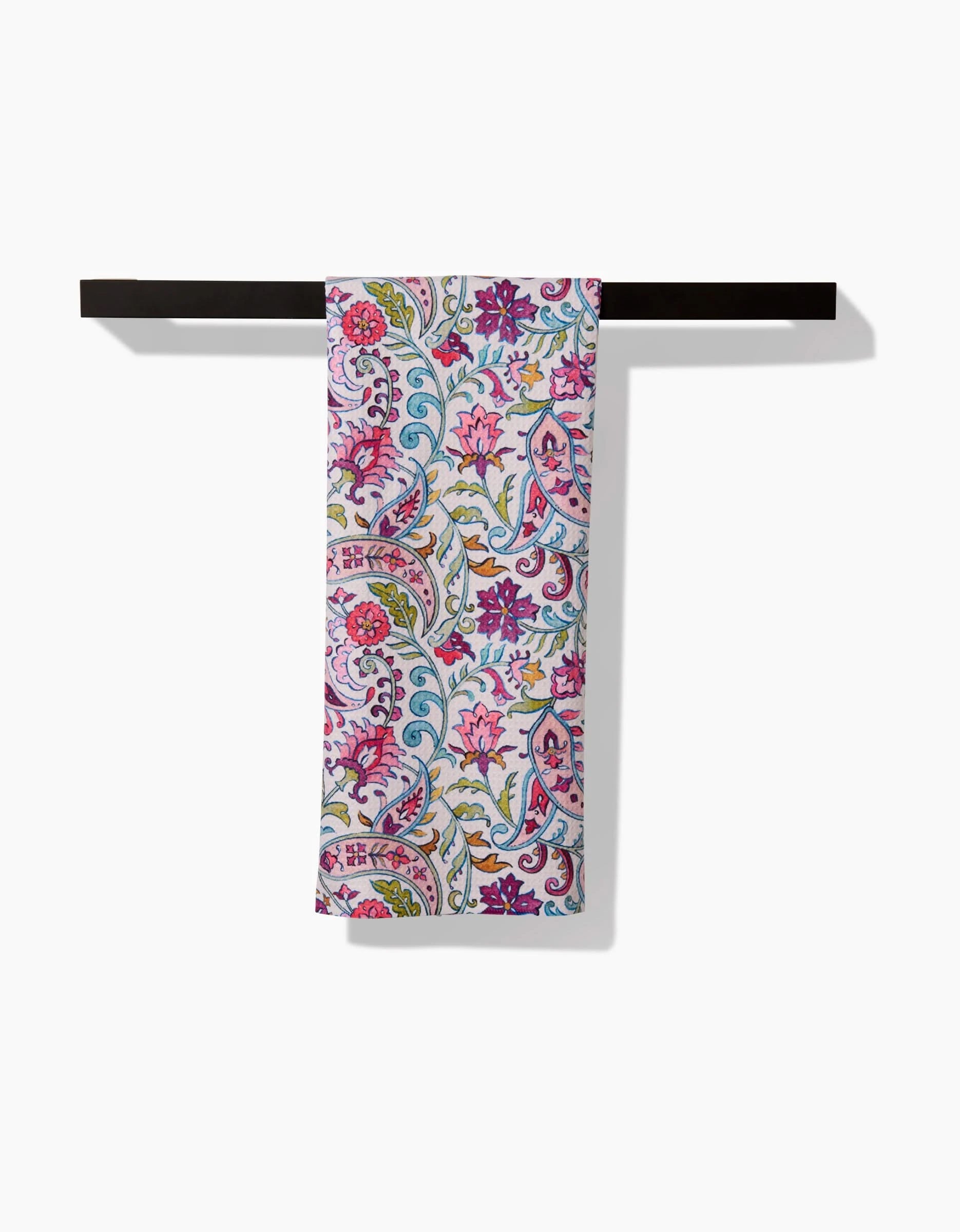 The Bazaar kitchen tea towel by Maayan Alper-Swan features a vibrant floral and paisley pattern in pink, purple, blue, and green on white. Made from soft Geoweave fabric for excellent absorbency, it hangs neatly on a dark towel bar against a white background.