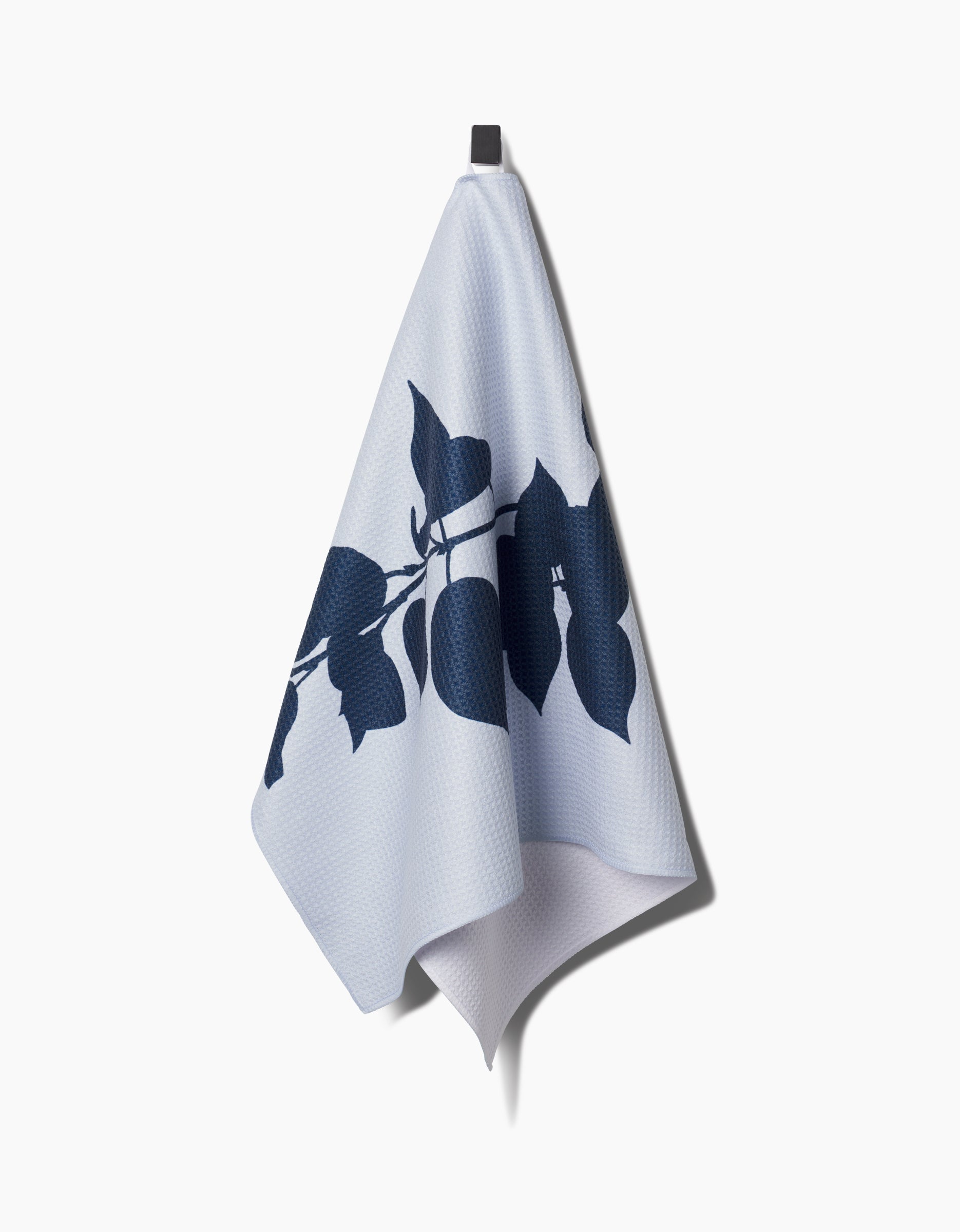 The PrintedPlant Birch tea towel, made from durable Geoweave fabric, features a dark blue leaf and branch pattern on light blue and hangs from a black hook against a white background.