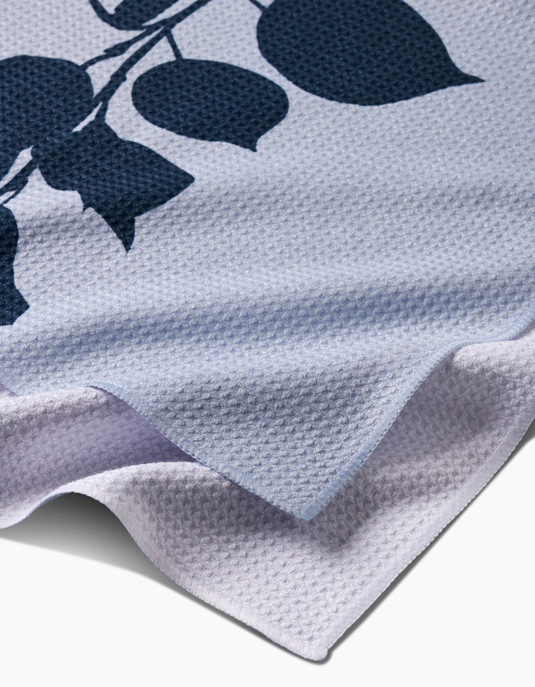 A close-up of PrintedPlants Birch tea towel, crafted from textured light purple Geoweave fabric with a dark blue leaf and branch design, shown folded at the corner.