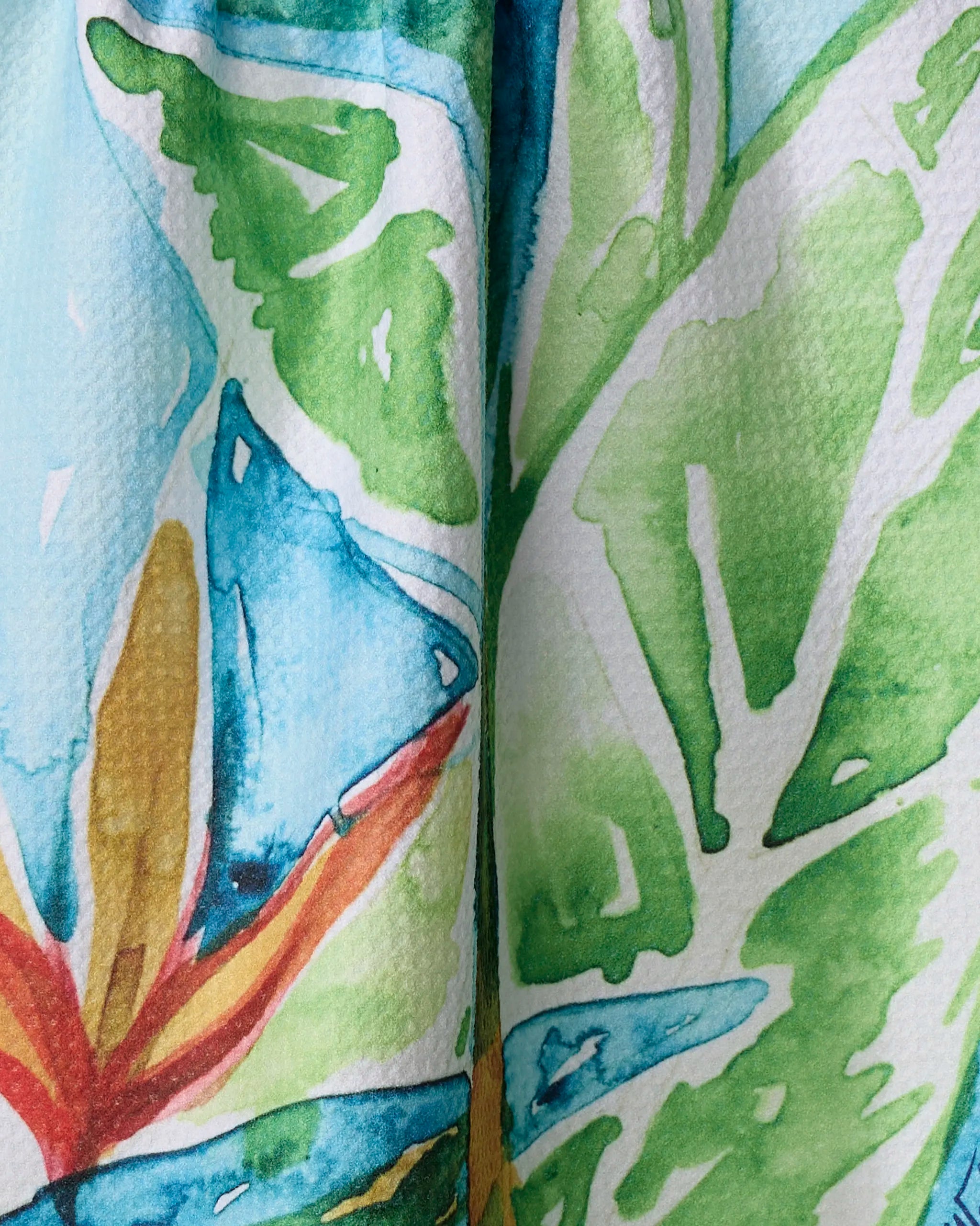A close-up of "Bird Of Paradise" by Skye Walker shows vibrant green, blue, yellow, and orange abstract shapes with white outlines—perfect inspiration for a kitchen tea towel made from recycled materials.