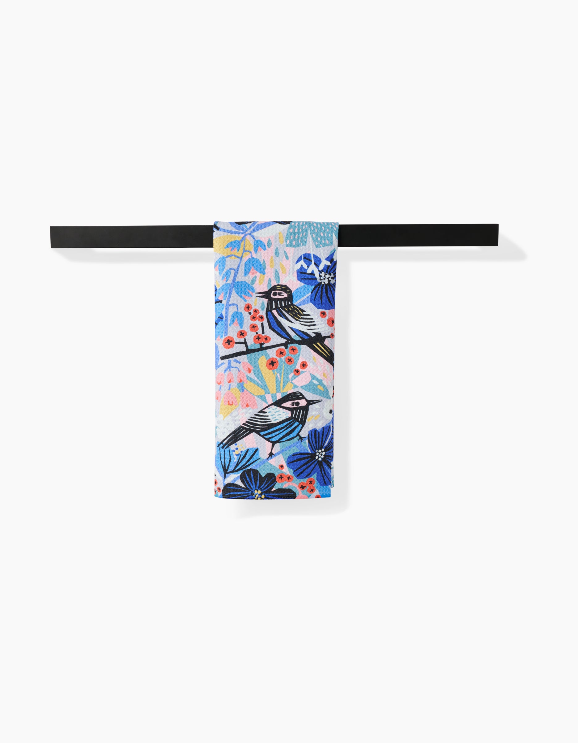The Masha Volnova Birds And Berries tea towel, made from premium Geoweave fabric and featuring a vibrant bird and floral design, hangs neatly folded over a sleek black bar against a white background.