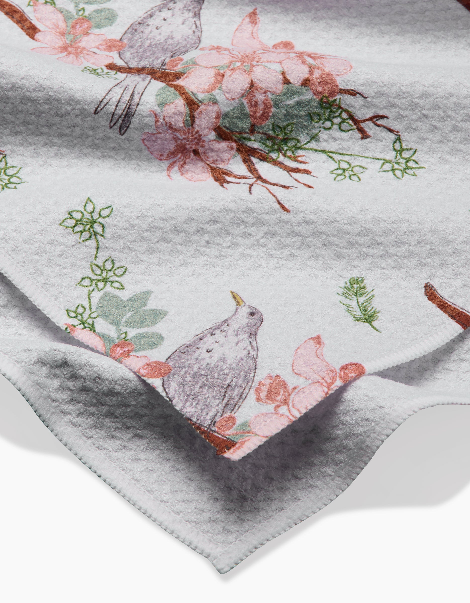 A close-up of the Linda Fox Blackbird and Blossom Geoweave fabric, featuring birds on branches amid pink flowers and green leaves.