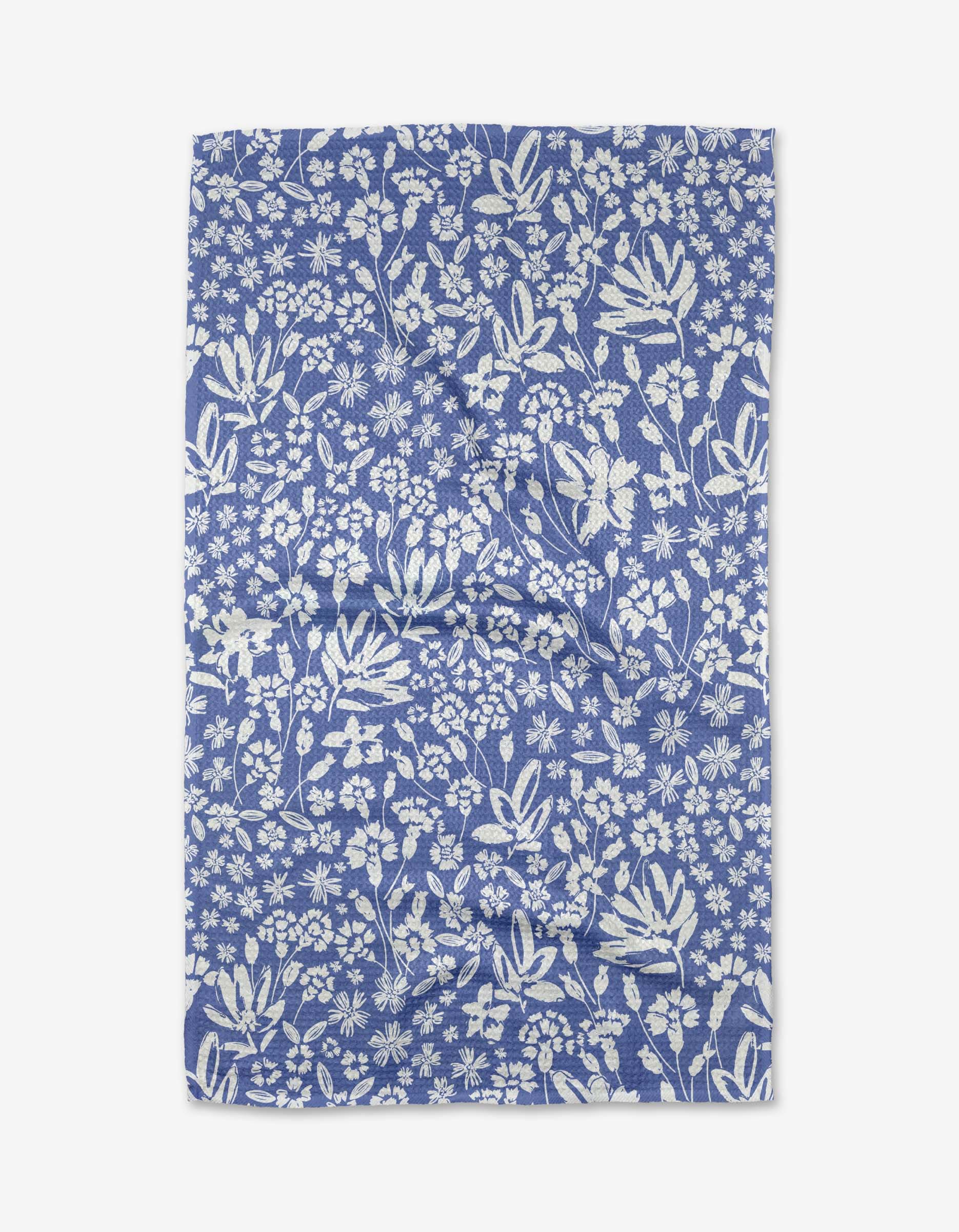 The Hufton Studio Bloom Me Over Floral tea towel is blue, made from recycled materials, and features a white floral and leafy pattern uniformly spread across Geoweave™ fabric.