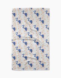 The Blue Heron tea towel by Elisabeth Wing showcases blue herons among orange leafy branches, arranged in a diagonal pattern across white eco-friendly fabric.