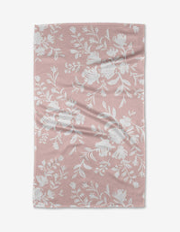 The Botanical Silhouettes Blush tea towel by Danelys Sidron features a pink textured fabric with a white floral pattern and gentle creases. Quick-drying, it’s a practical and stylish addition to any kitchen.