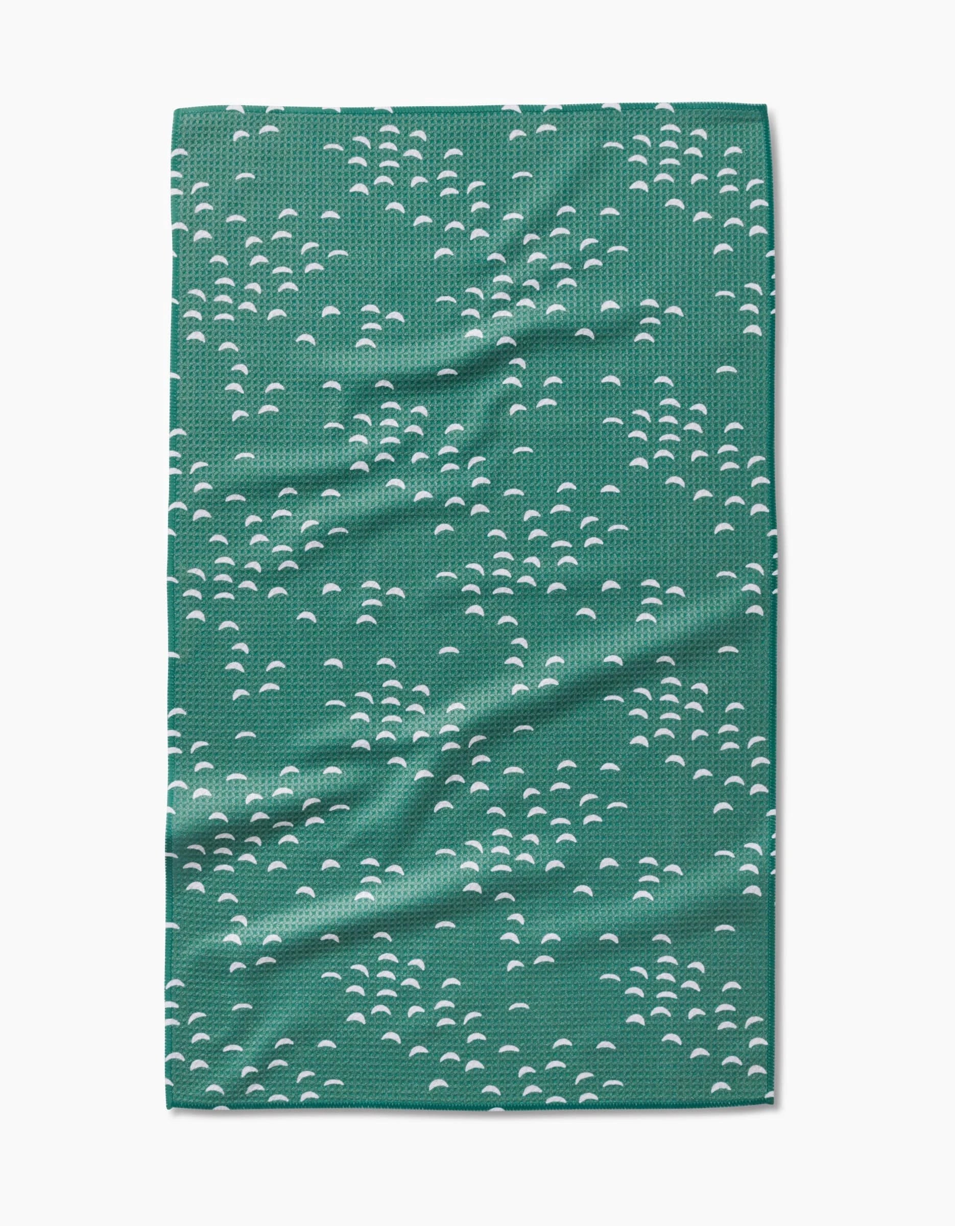 The Breezeway tea towel by Jessica Swift features a repeating pattern of small white semi-circular shapes on green, made with ultra-absorbent Geoweave fabric. The towel is shown flat with slight wrinkles visible.