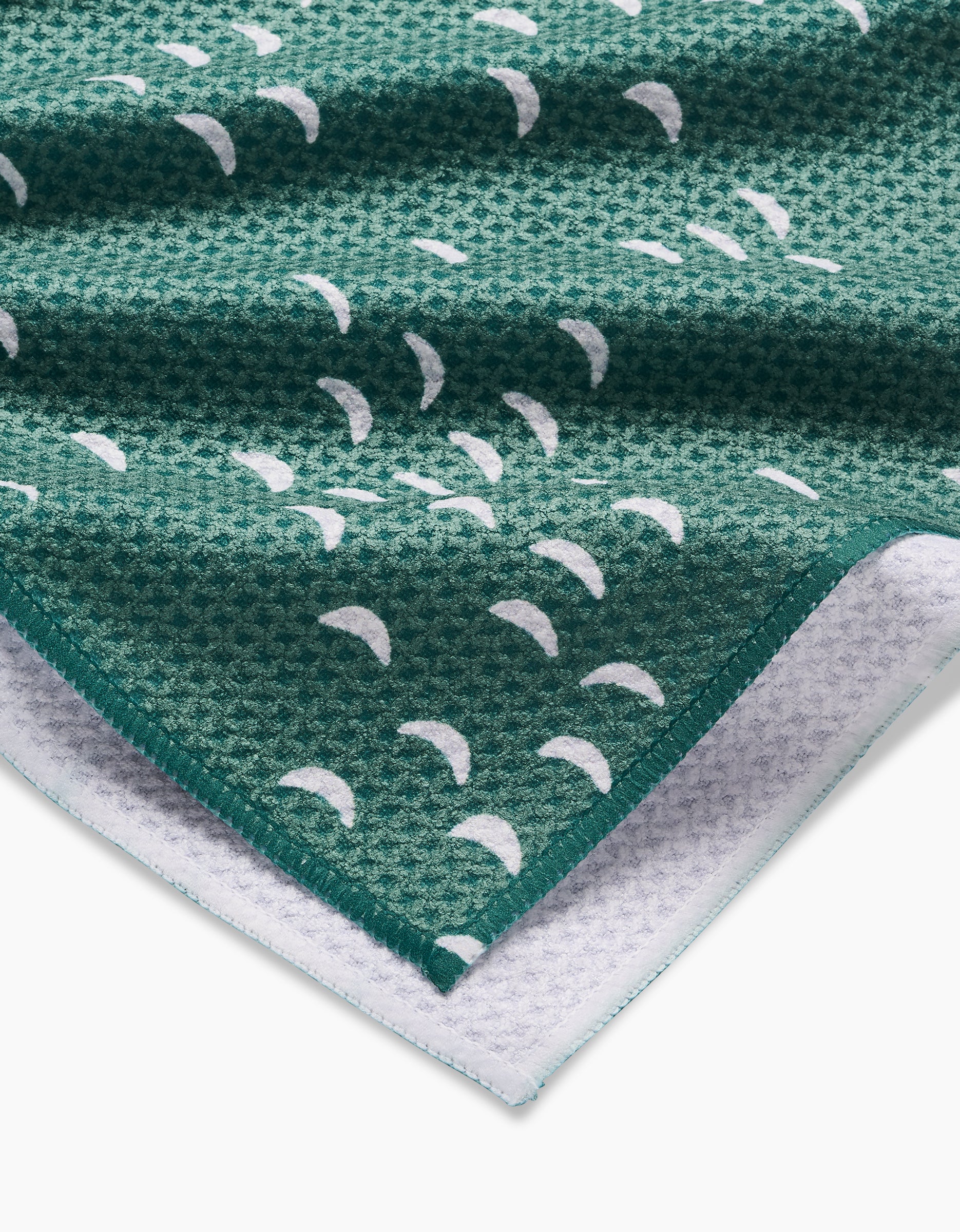 Close-up of textured green Breezeway Geoweave fabric by Jessica Swift, with white crescent shapes and a folded corner showing both the patterned front and white underside of this ultra-absorbent tea towel.