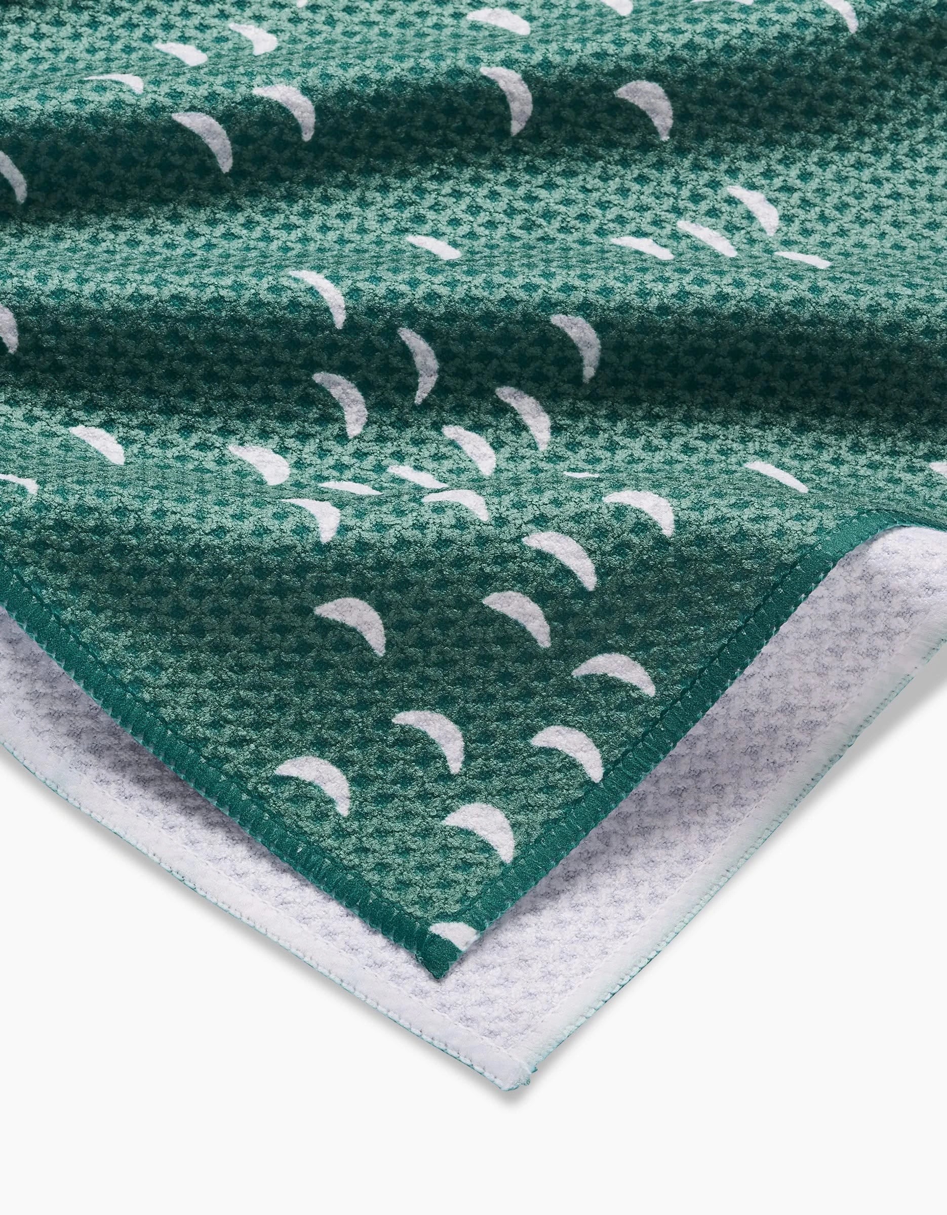 Close-up of textured green Breezeway Geoweave fabric by Jessica Swift, with white crescent shapes and a folded corner showing both the patterned front and white underside of this ultra-absorbent tea towel.