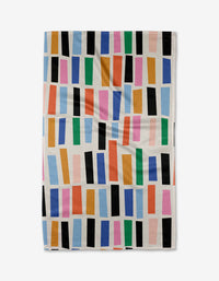 The Bricks kitchen towel by Jennifer Bouron is white, made from recycled fabric, and features colorful staggered rectangles in blue, green, orange, pink, and black. The slightly wrinkled towel is shown against a plain background.