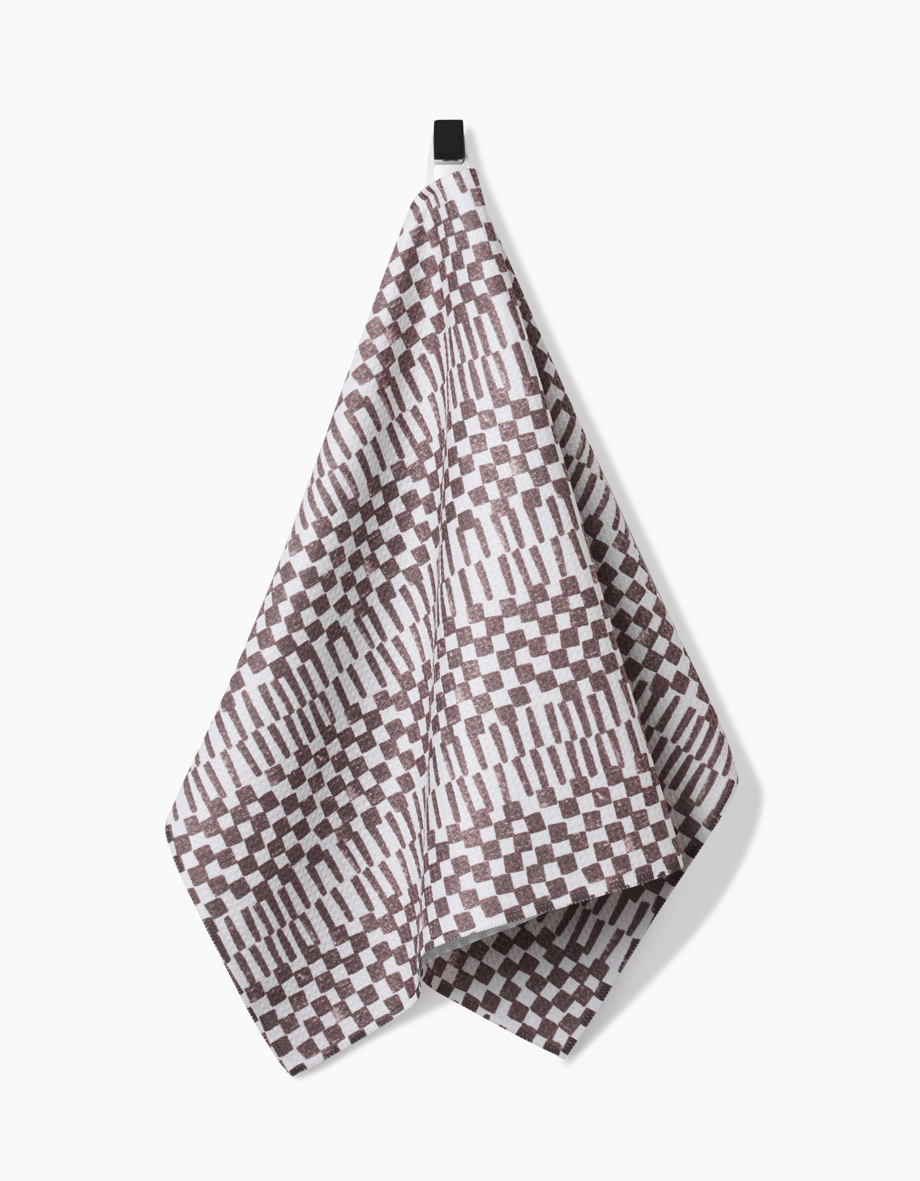 The Chutes Coffee tea towel by Studio Jeannot showcases a geometric brown and white pattern of rectangles and checks, made from Geoweave fabric, and hangs by a black loop on a white background.