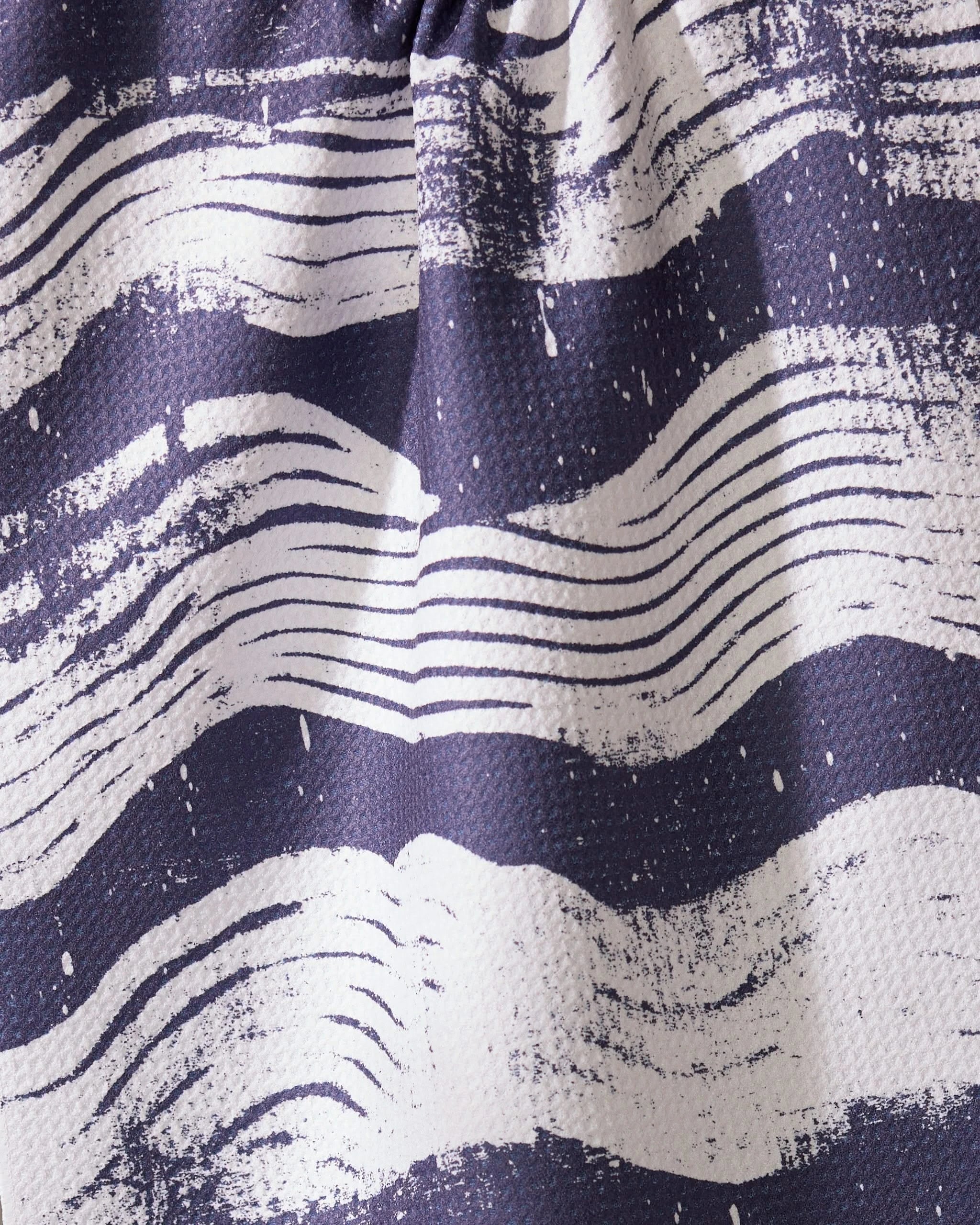 A close-up of Geometrys Brushline Navy tea towel, featuring quick-drying fabric and wavy, hand-drawn white stripes on a dark blue background for a dynamic, artistic texture.