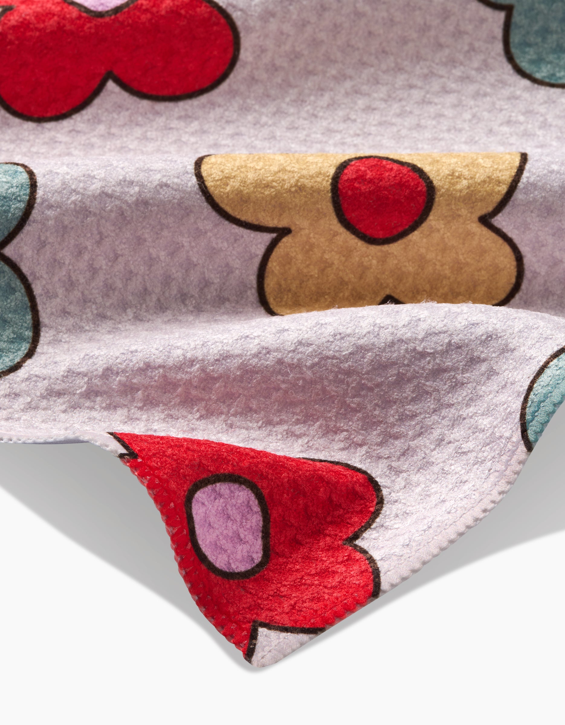 A close-up of Purely Kaylie’s Buttercream Blossoms tea towel shows soft, ultra-absorbent Geoweave™ fabric with colorful abstract floral shapes on a light background and folded edges revealing red, blue, tan, and purple designs.