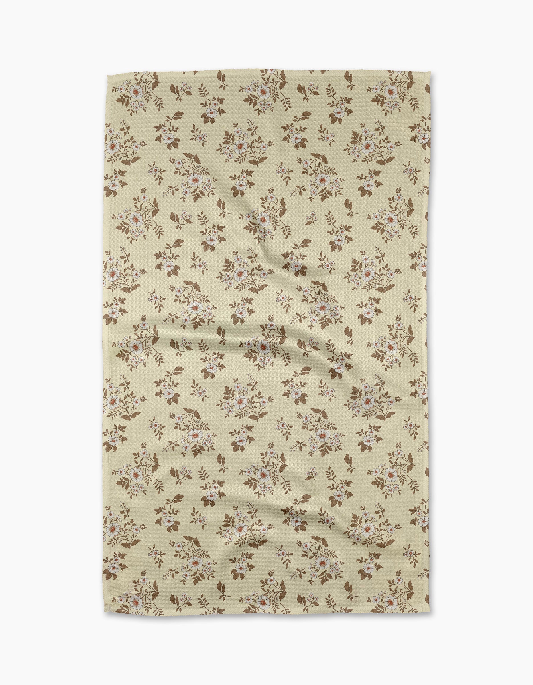 The Buttercream Primrose kitchen tea towel by Danelys Sidron features a beige base with subtle brown and mauve floral prints. Shown flat with light creases on a white background, it's eco-friendly and crafted from recycled materials.