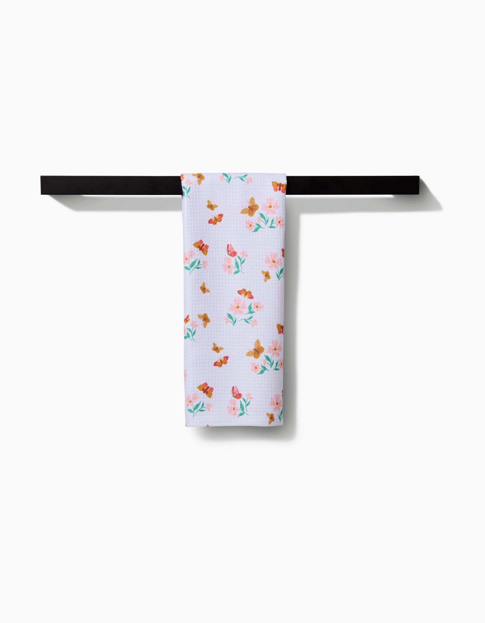 The Butterfly Garden Tea Towel by Danelys Sidron, featuring a vibrant floral design on Geoweave™ fabric, is elegantly displayed over a modern black towel bar against a white background.