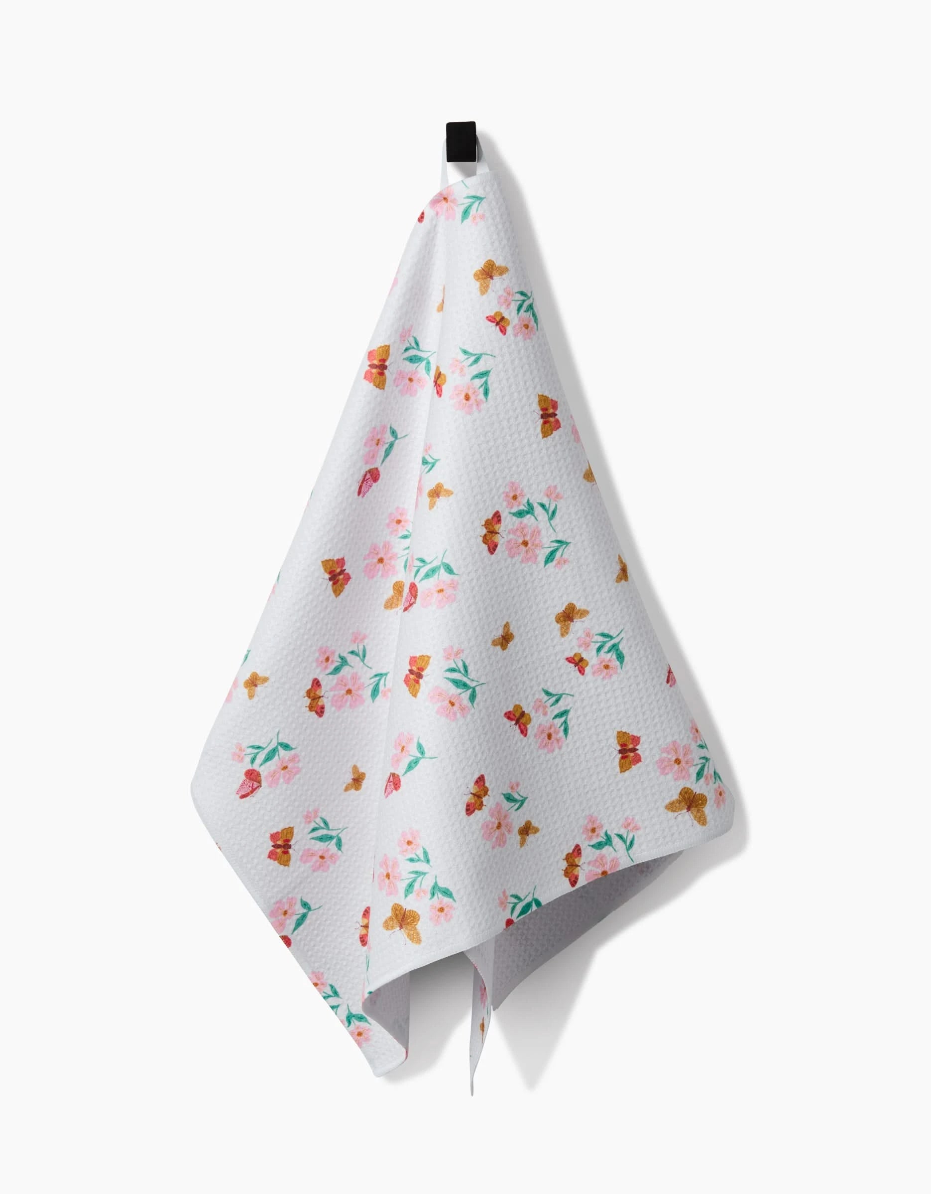 The Danelys Sidron Butterfly Garden Tea Towel, made from Geoweave™ fabric, displays vibrant floral and butterfly patterns and hangs from a black hook against a plain white background.