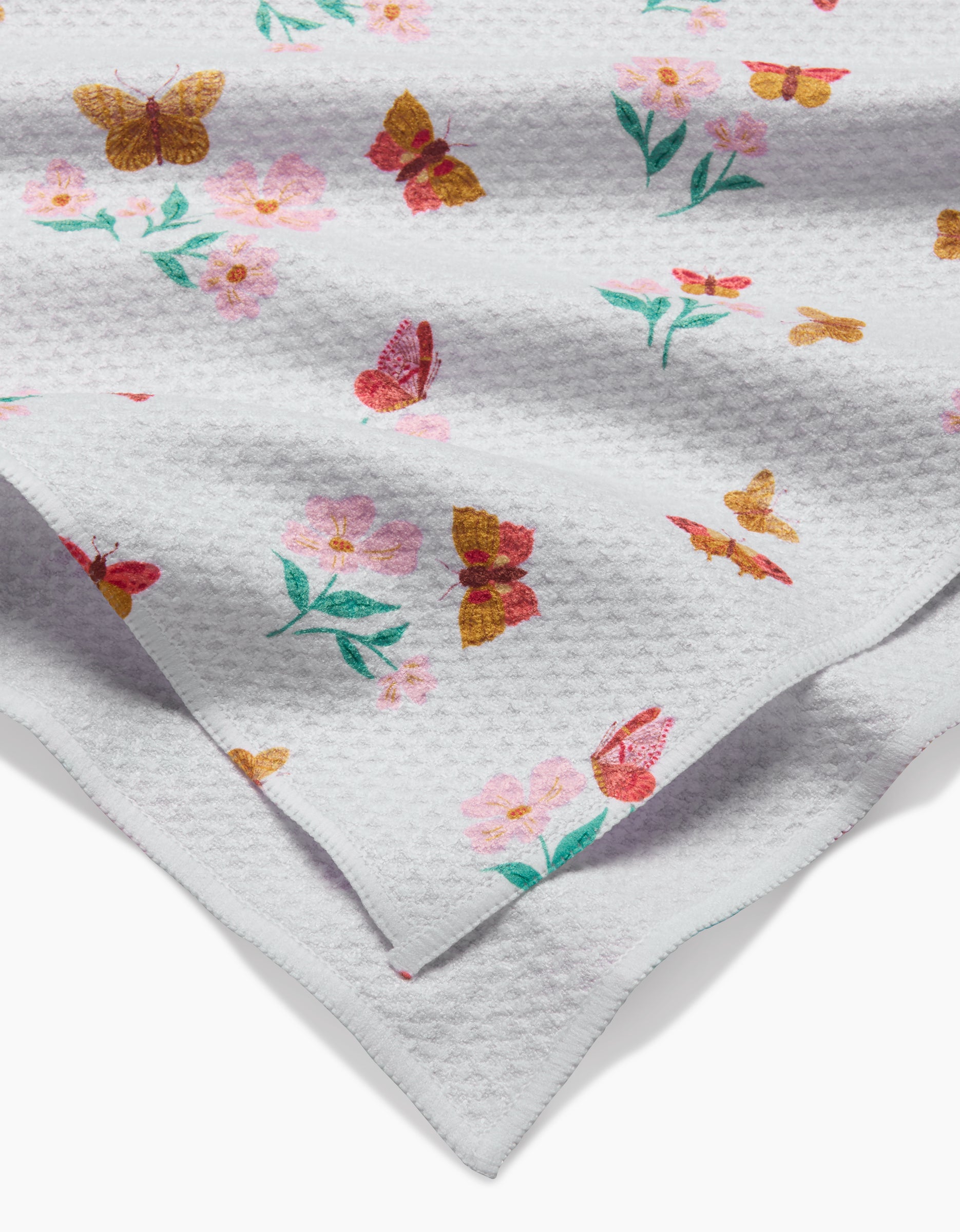 A close-up of the Butterfly Garden Tea Towel by Danelys Sidron, made with textured Geoweave™ fabric, displays colorful butterflies and pink flowers with green leaves on both sides.
