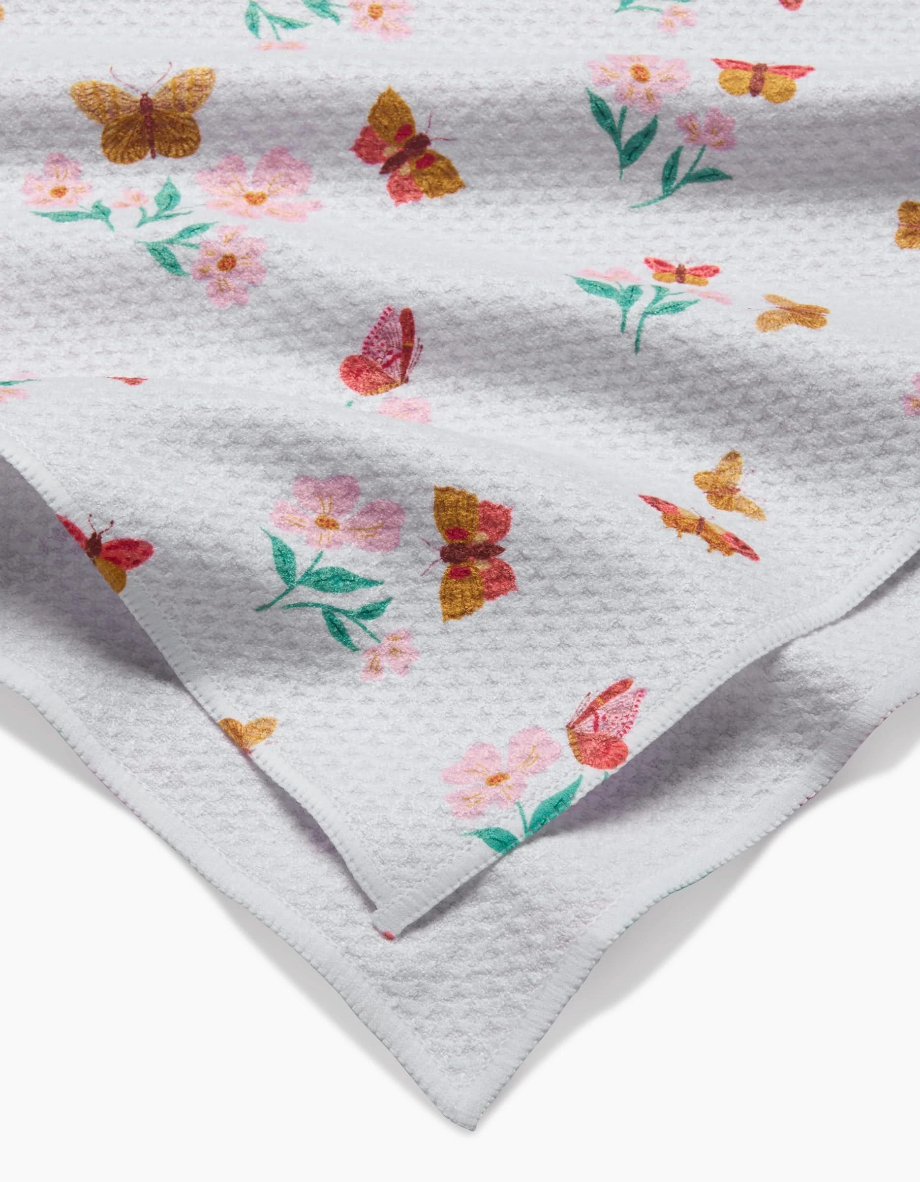 A close-up of the Butterfly Garden Tea Towel by Danelys Sidron, made with textured Geoweave™ fabric, displays colorful butterflies and pink flowers with green leaves on both sides.