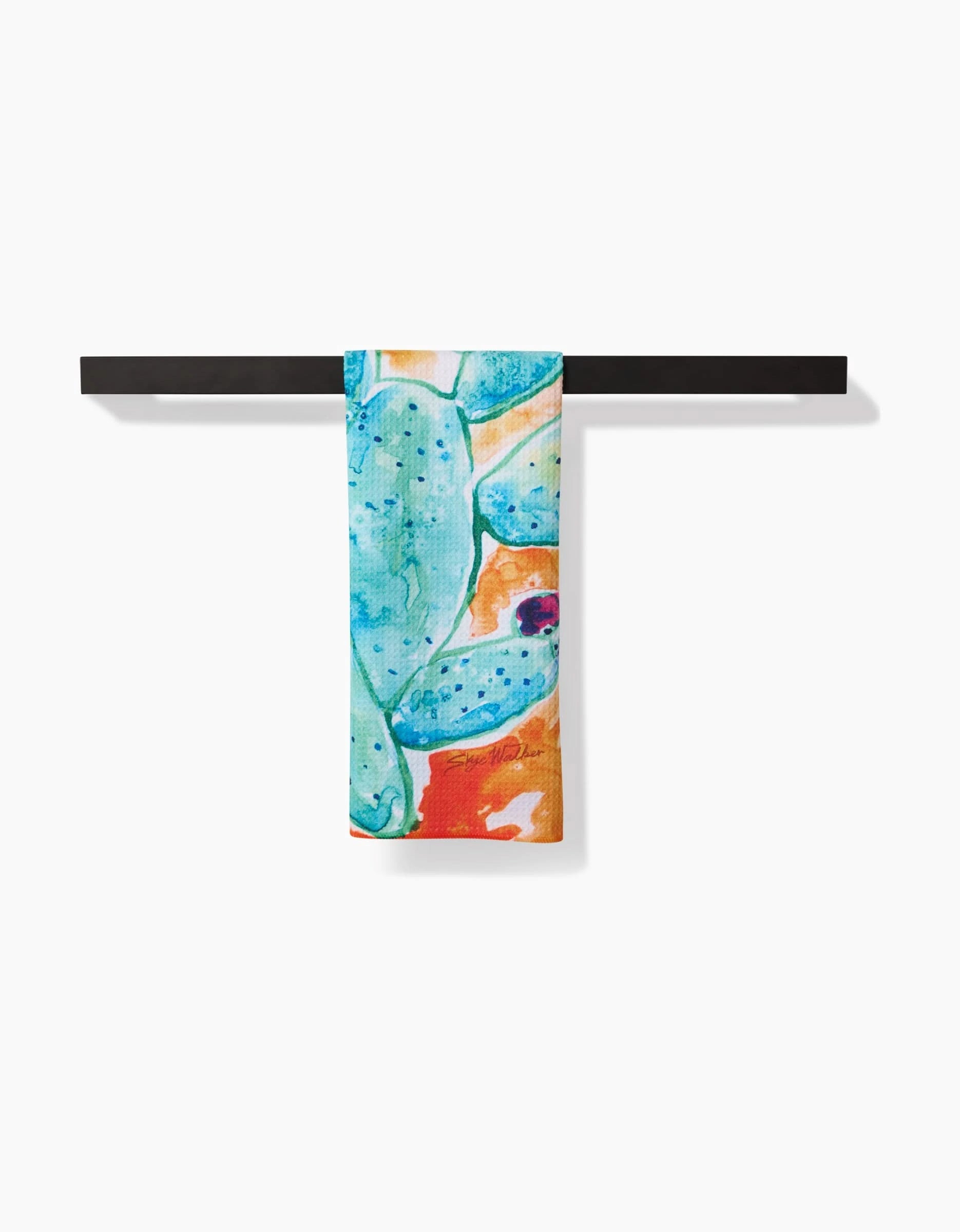 The Skye Walker Cacti tea towel, featuring a blue and green cactus design on Geoweave fabric, hangs neatly over a black horizontal towel bar against a white background.
