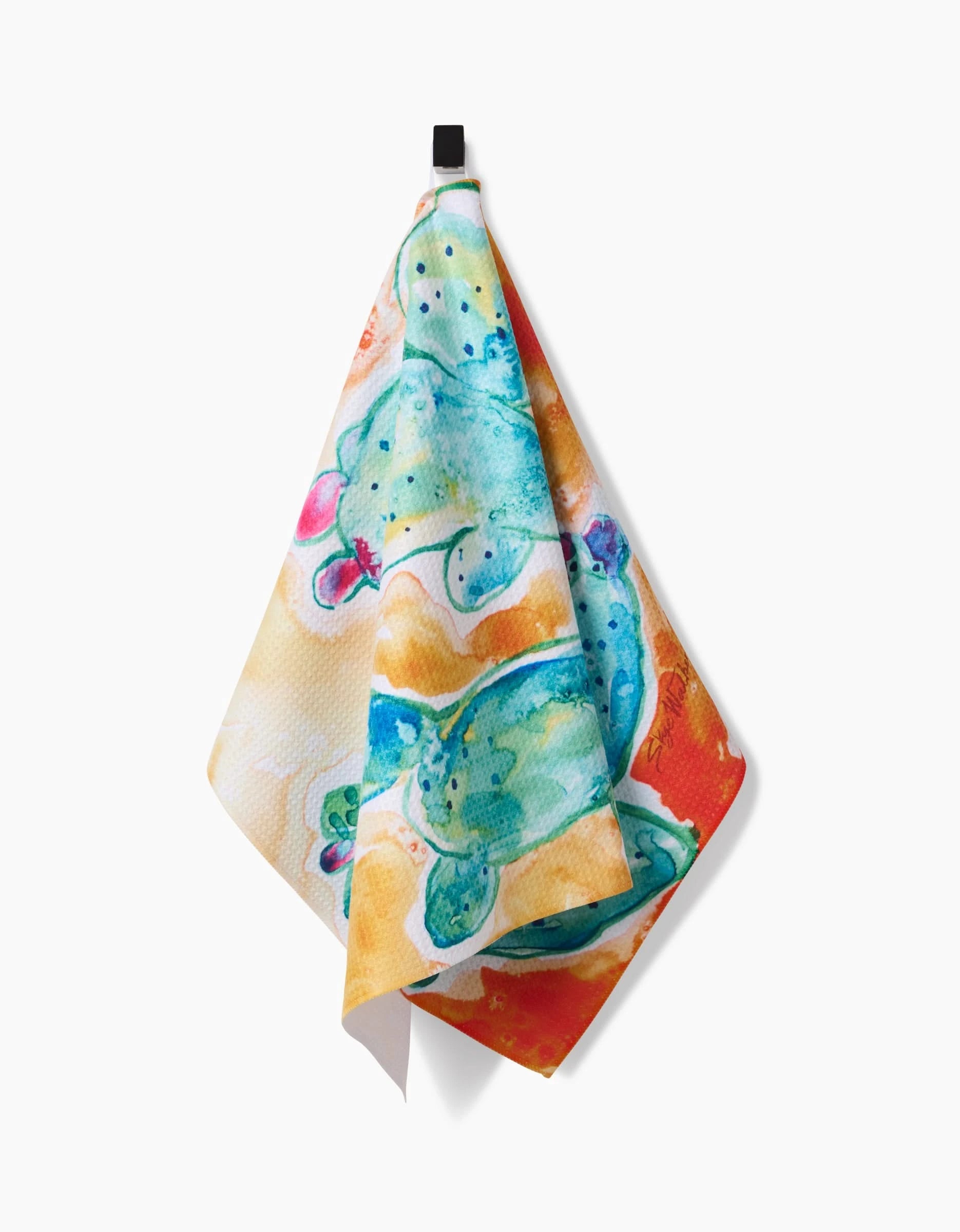 The Skye Walker Cacti tea towel features a vibrant watercolor print of green cacti with pink flowers, shown hanging from a black hook on a white background.
