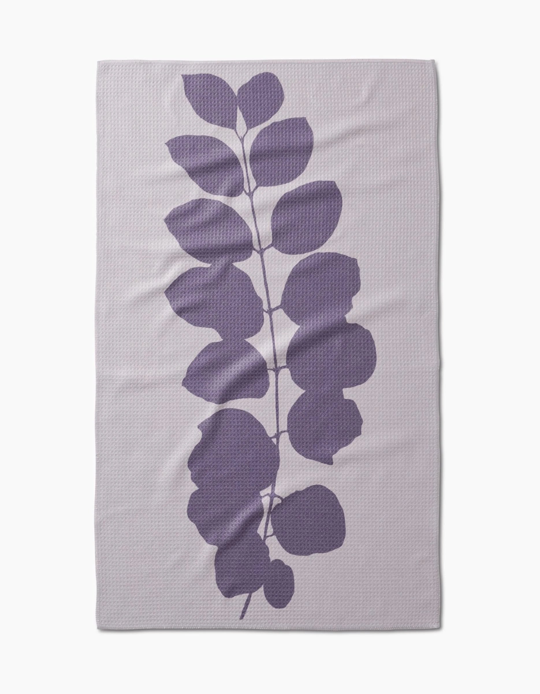 The PrintedPlant Carob blanket is light gray, rectangular, and made from ultra-absorbent Geoweave fabric. It features a large central purple leafy branch with rounded leaves on a subtly textured background.