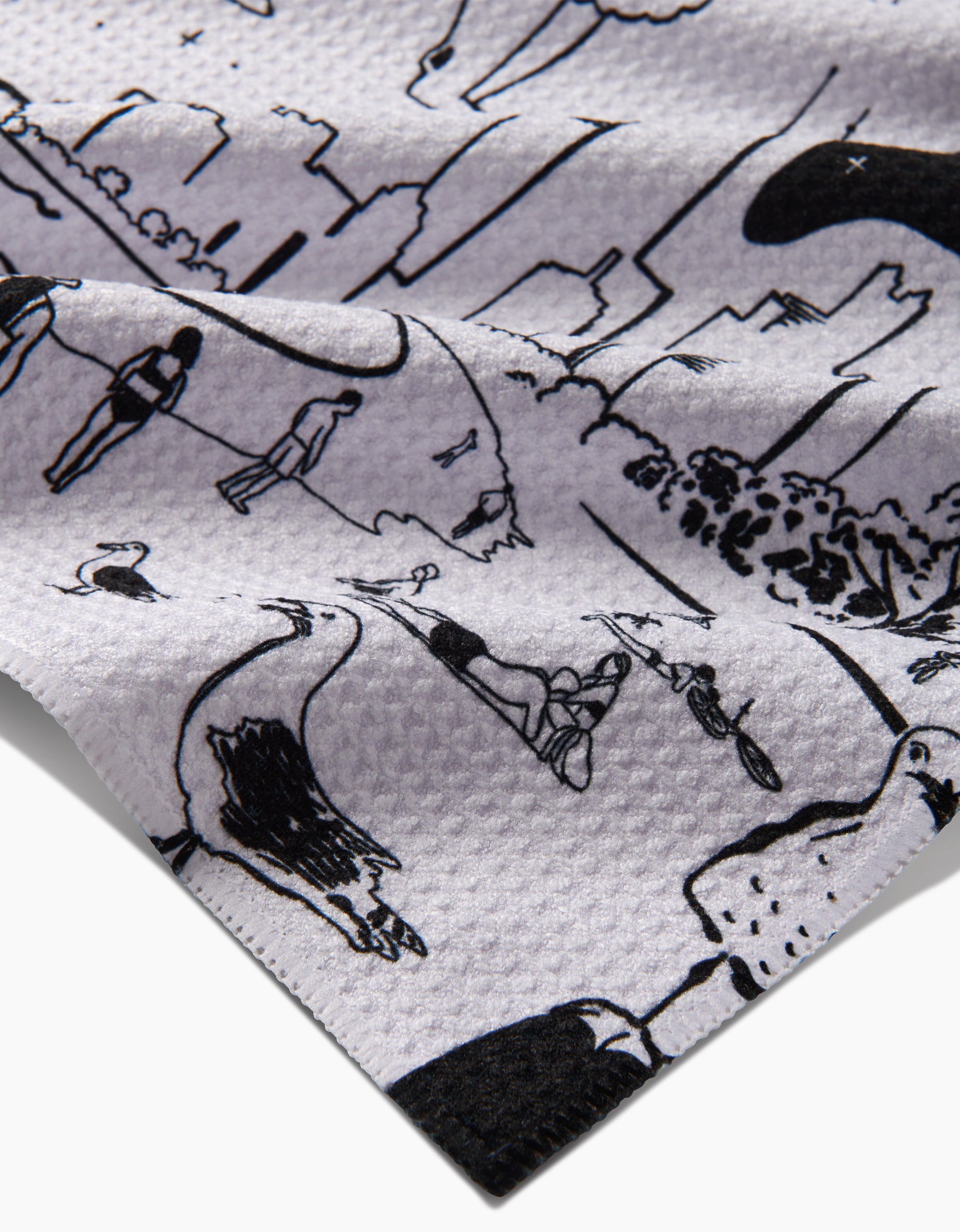 A close-up of the Chicago Tea Towel by Elisabeth Wing, made from recycled Geoweave fabric, featuring black line drawings of people walking, cycling, trees, and a city skyline.