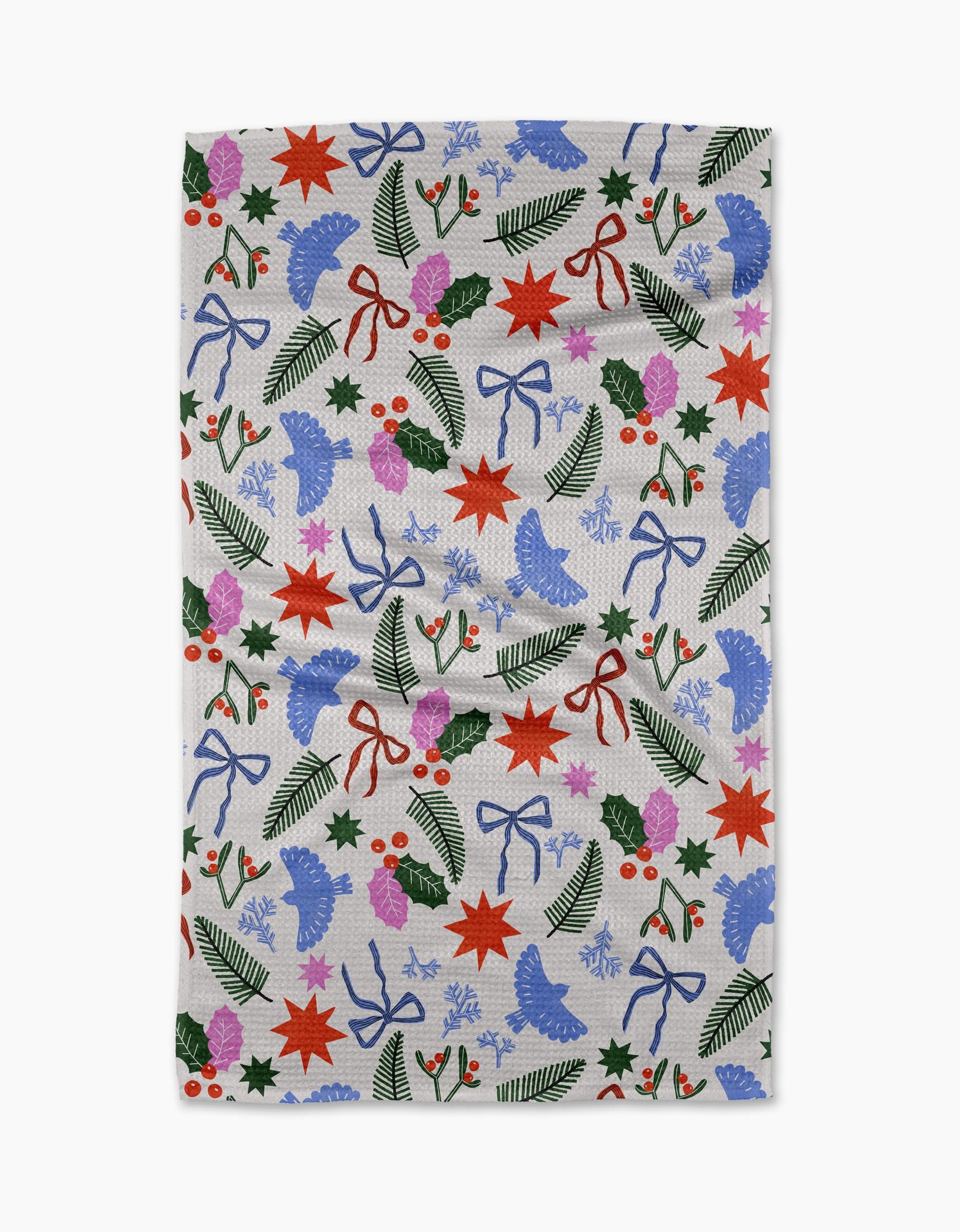 Add festive cheer to your kitchen with Claire Iglesias Christmas Garden Party recycled towel, featuring colorful stars, bows, pine branches, holly, pinecones, and flowers—perfect for brightening up holiday dish duty.