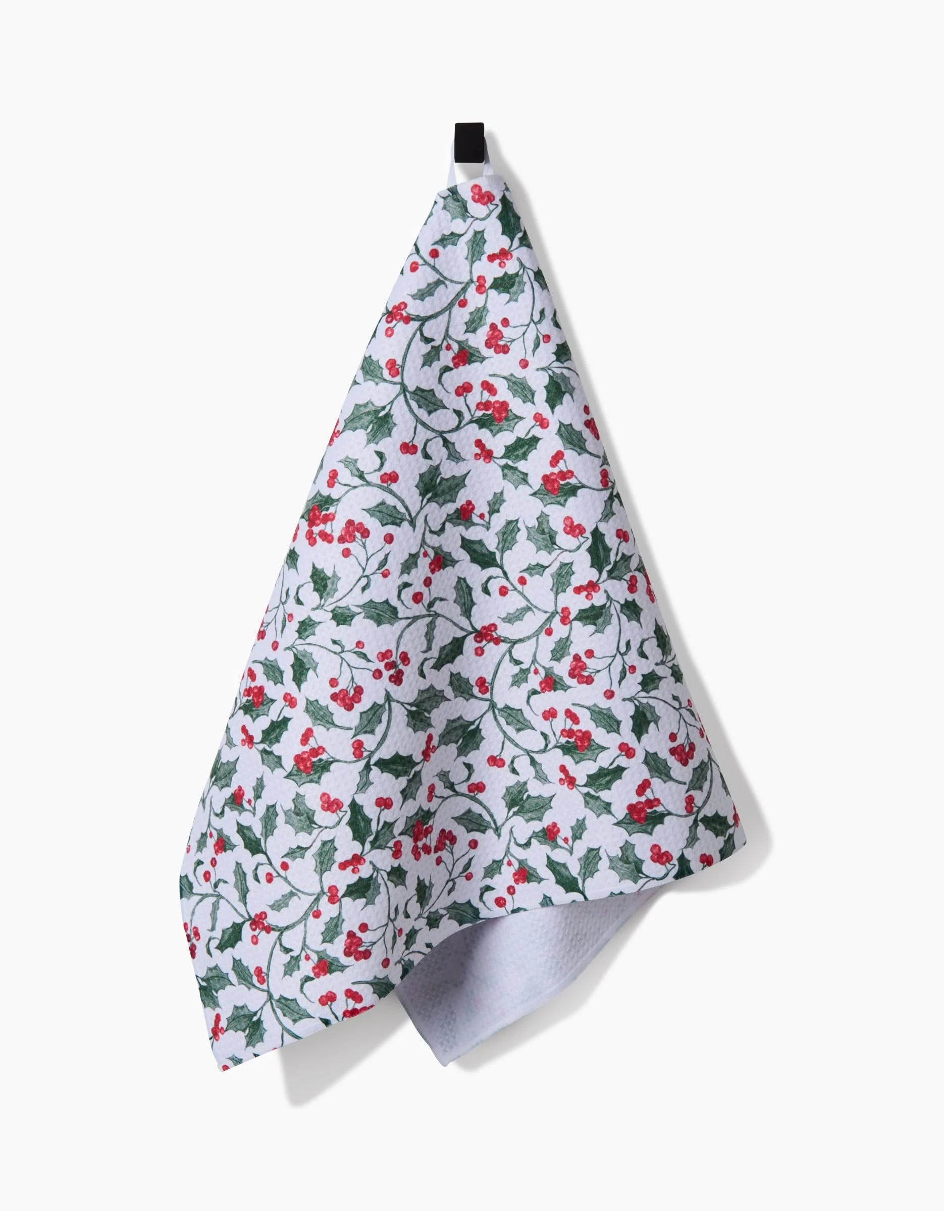 The Aubrey Fairchild Christmas Holly tea towel features green holly leaves and red berries, hanging from a black loop against a plain white background.