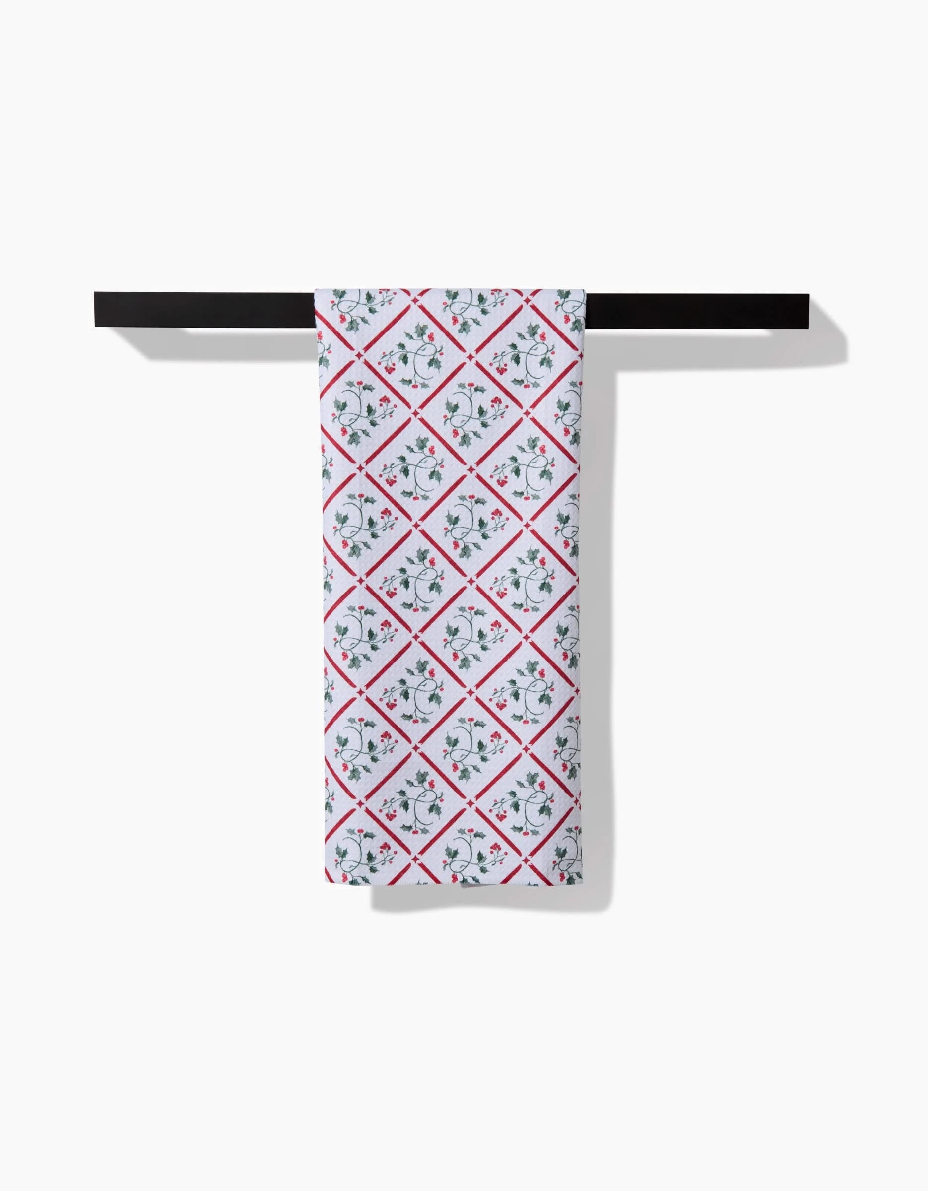 An Aubrey Fairchild Christmas Mistletoe Trellis tea towel hangs on a black rod, displaying blue and red floral diamond patterns printed across the white Geoweave fabric.