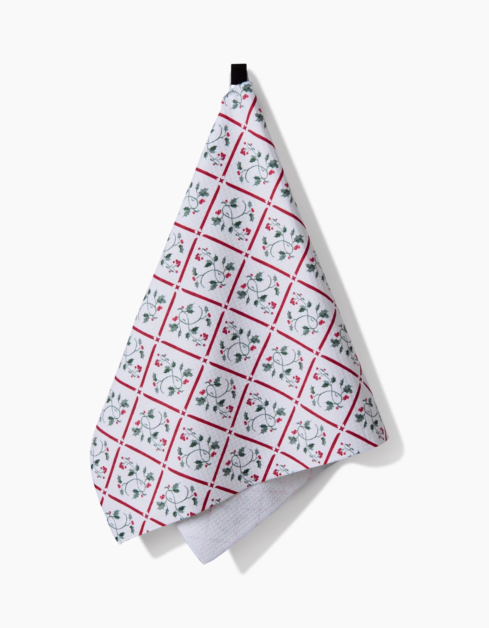 The Aubrey Fairchild Christmas Mistletoe Trellis tea towel, made from absorbent Geoweave fabric, features a red grid and green floral design on white and hangs from a black loop against a plain white background.