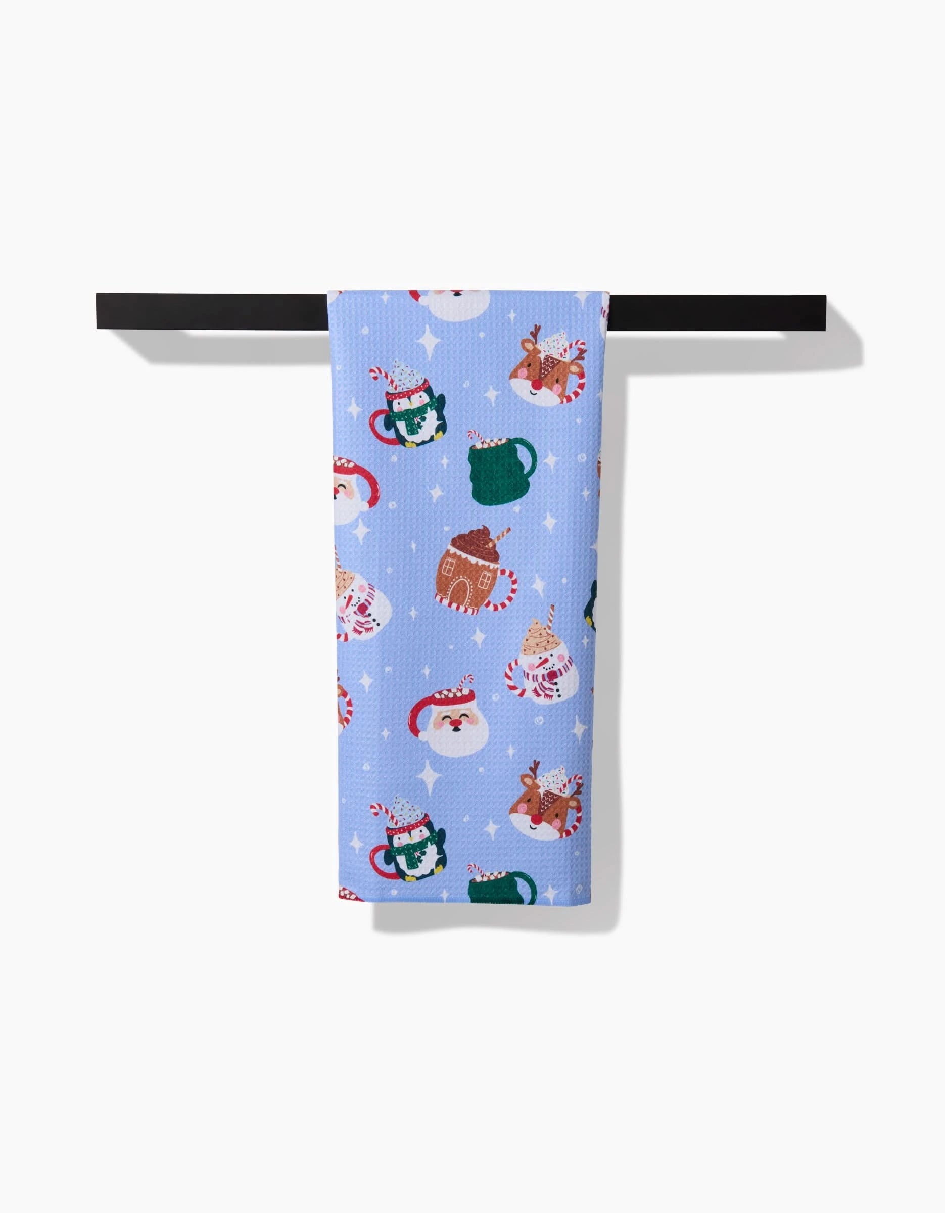 The Vaishali Design Studio Christmas Mugs blue recycled tea towel hangs on a black rod, featuring festive patterns like Santa faces, reindeer, mugs, candy canes, and white snowflakes.