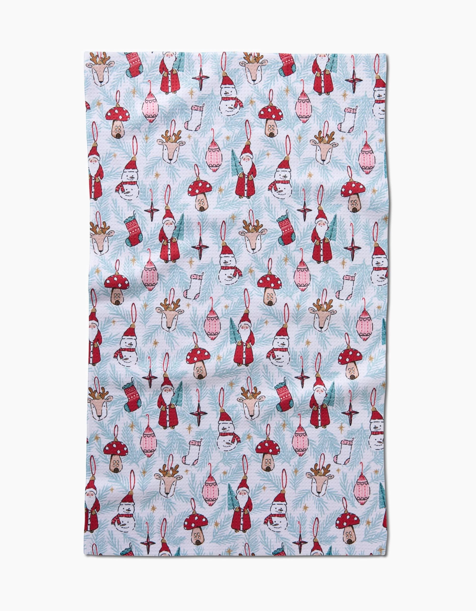 The Christmas Traditions recycled kitchen towel by Hufton Studio features a festive light blue design with Santa faces, mushrooms, gingerbread men, reindeer, mittens, ornaments, birds, and pine trees in cheerful holiday colors.