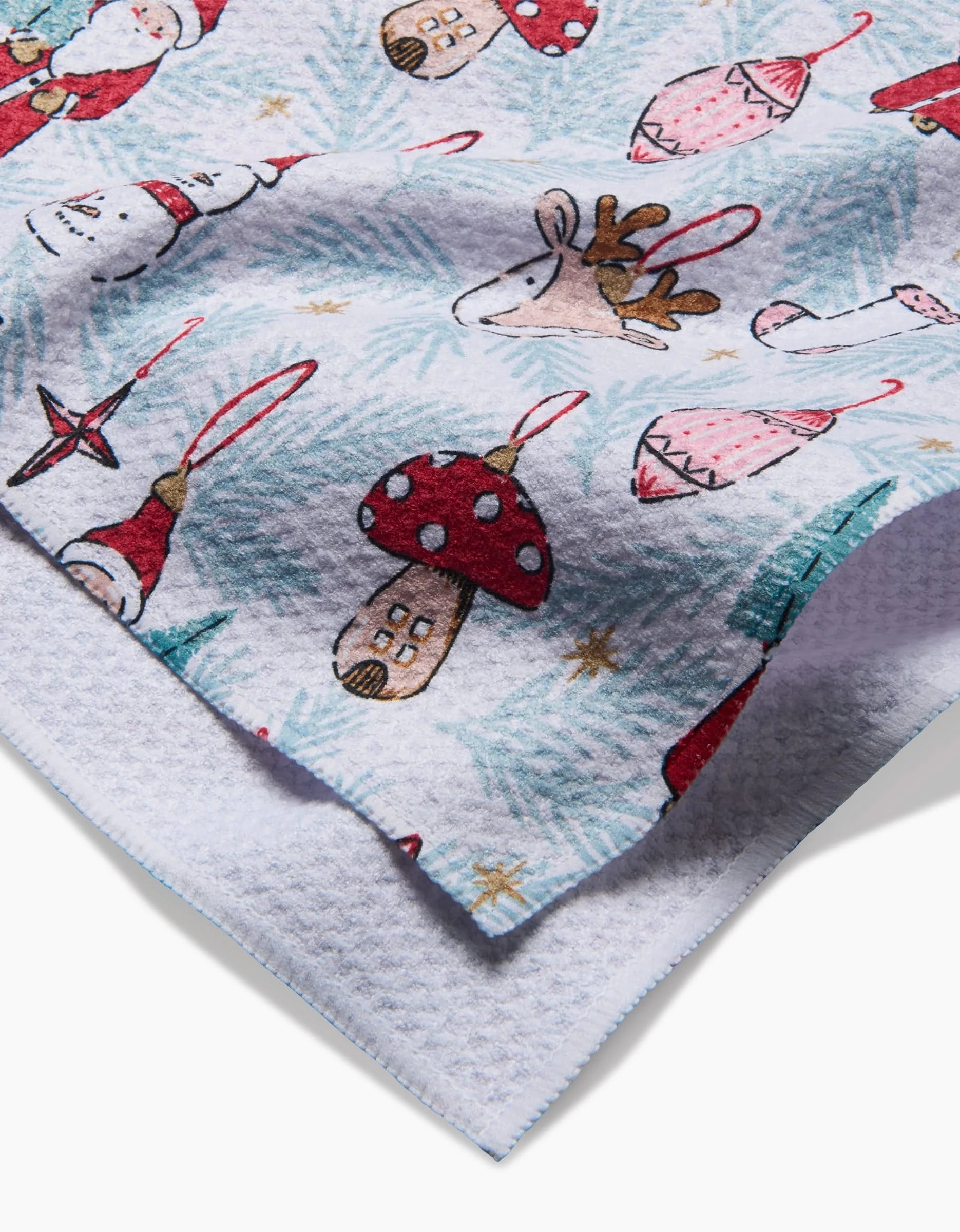 A close-up of the Hufton Studio Christmas Traditions towel, featuring ultra-absorbent texture and festive red, white, and beige prints—reindeer, mushrooms, snowmen, stars, and ornaments—on a light background.