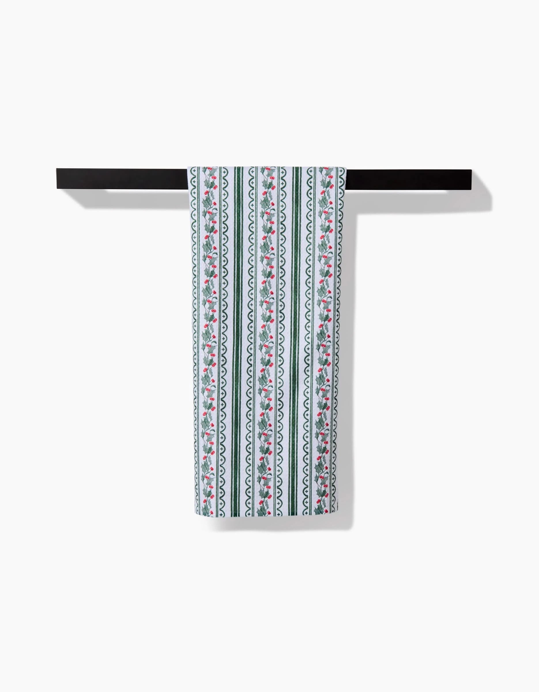 The Christmas Vines recycled kitchen towel by Aubrey Fairchild, with green, pink, and white vertical stripes featuring floral and wavy patterns, hangs on a black towel bar against a white background.