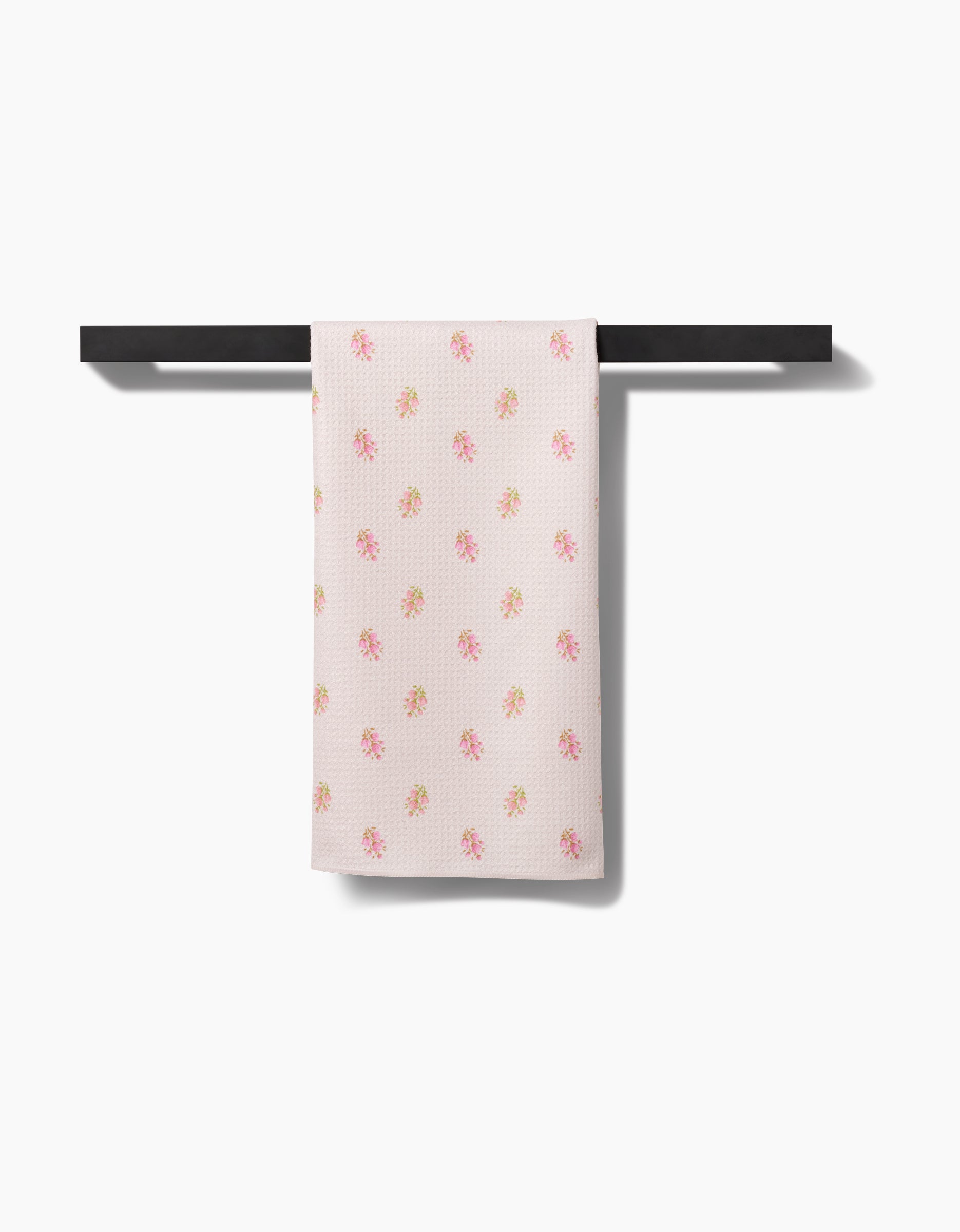 The Cindy Tea Towel by Kelsi Fullmer, featuring a pink and yellow floral design on Geoweave™ fabric, hangs over a black towel bar against a plain white background.