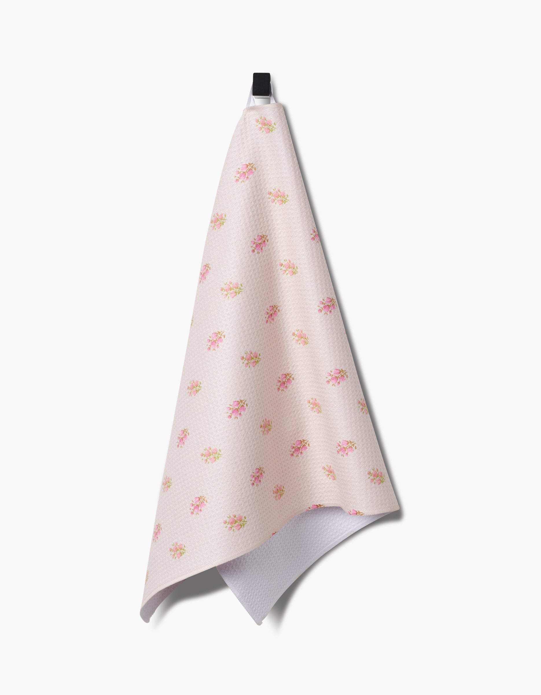 The Cindy tea towel by Kelsi Fullmer is crafted from recycled materials in pink, with a textured pattern and small floral designs in pink, yellow, and orange. It hangs from a black loop against a white background.