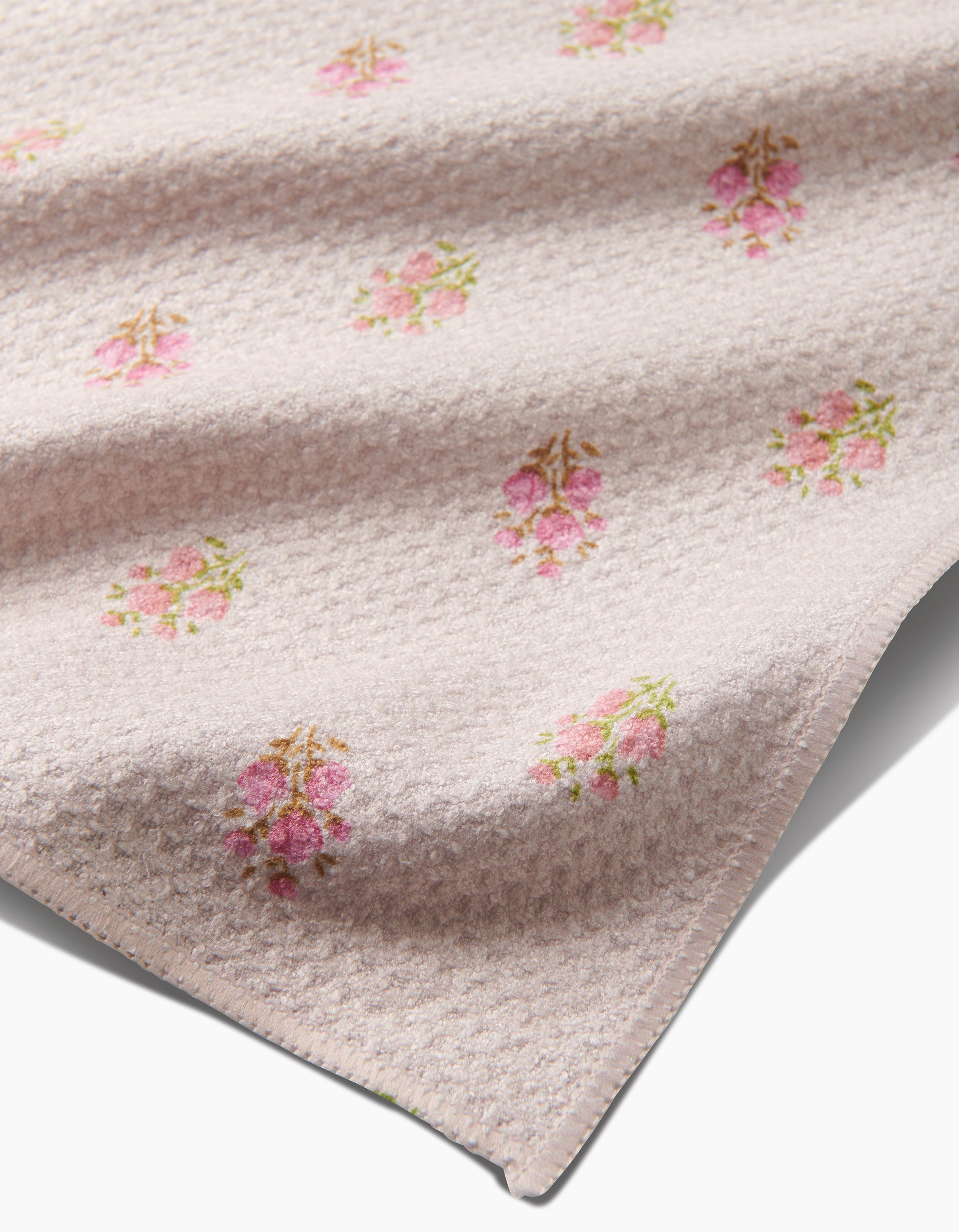 A close-up shows the Cindy tea towel by Kelsi Fullmer—a soft, textured light pink towel made from recycled materials, with a pattern of small pink floral bouquets and its edge visible in the foreground.