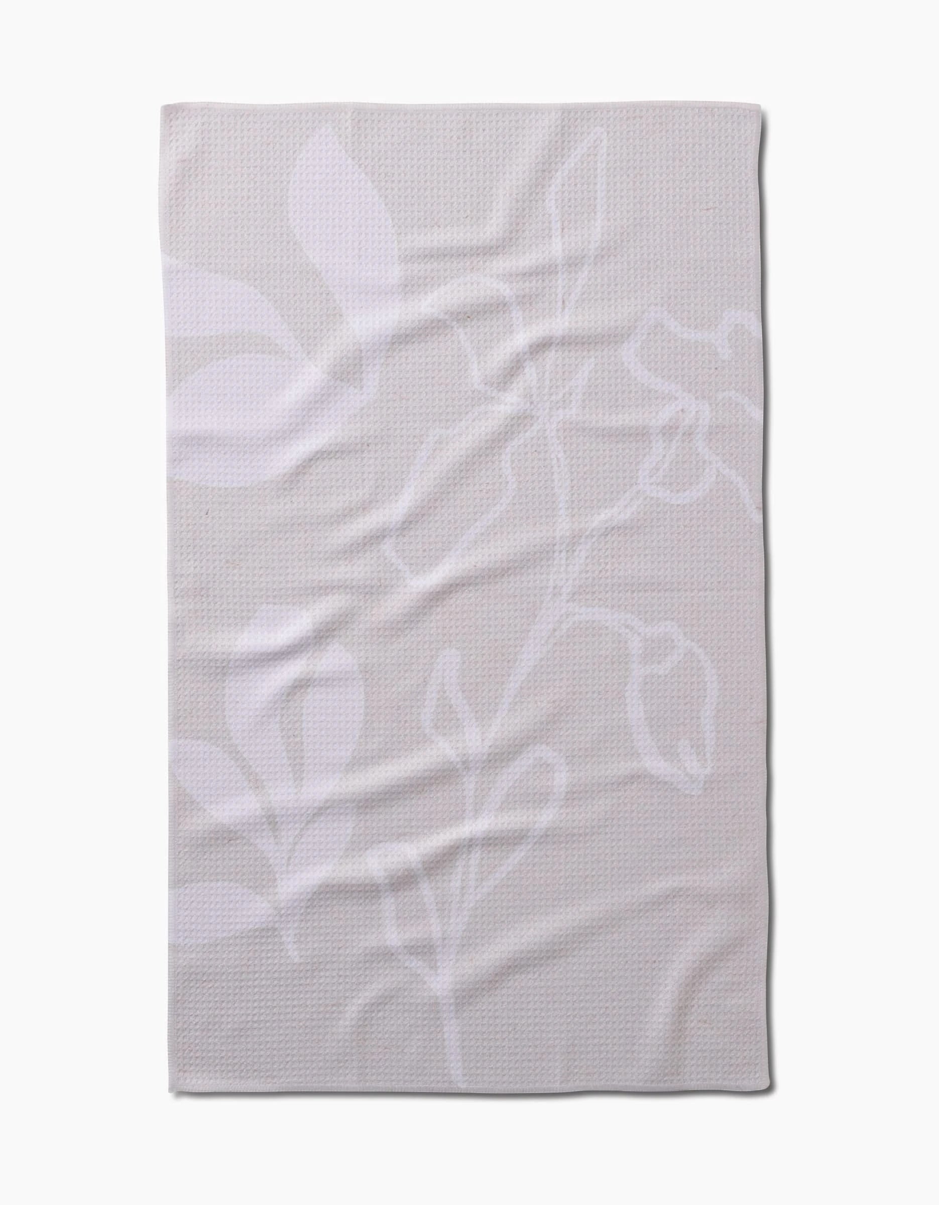 The GEOMETRY Clean blanket is beige with a subtle white floral pattern of large leaves and flower outlines, crafted from recycled materials. It is shown laid flat with gentle wrinkles visible.