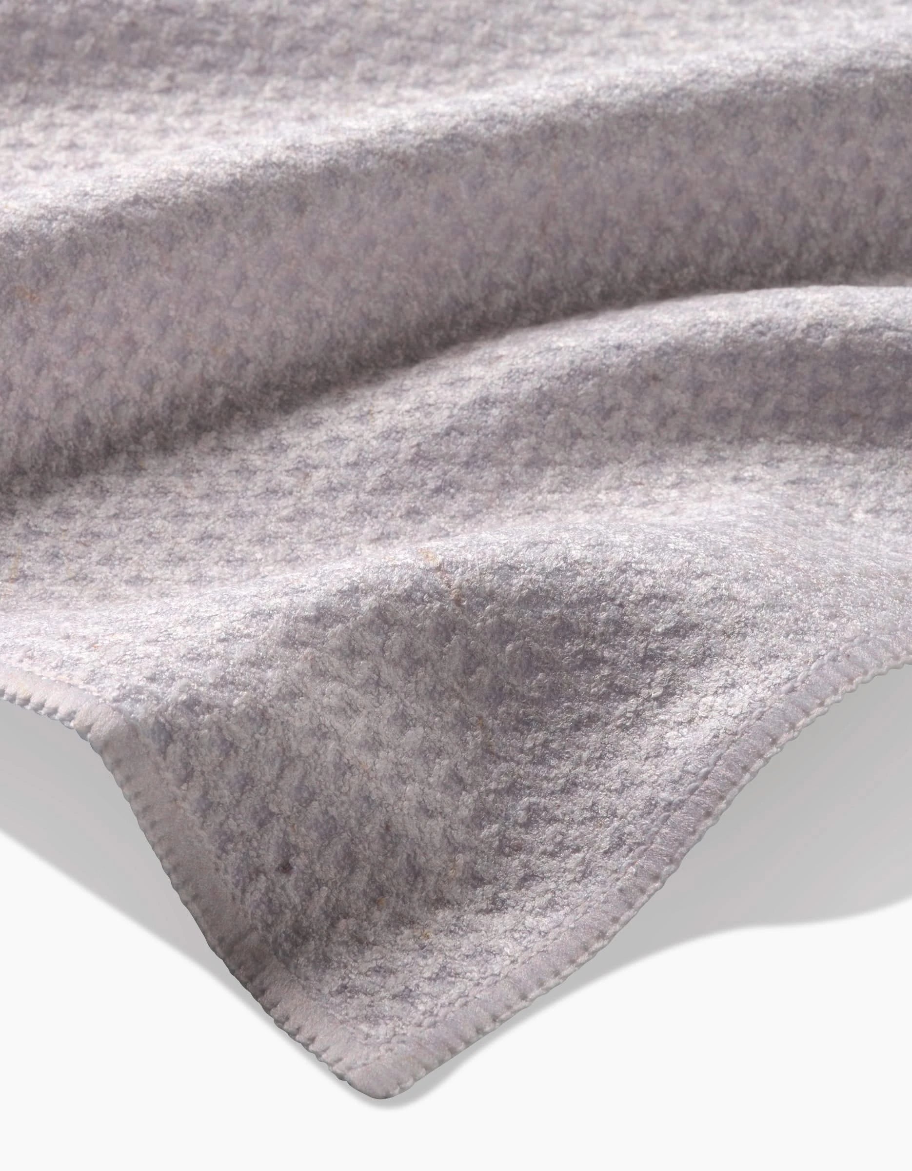 A close-up of Clean by GEOMETRY: a soft, light gray Geoweave tea towel with subtle raised patterns, curved folds, stitched edges, and an eco-friendly blend of recycled materials.