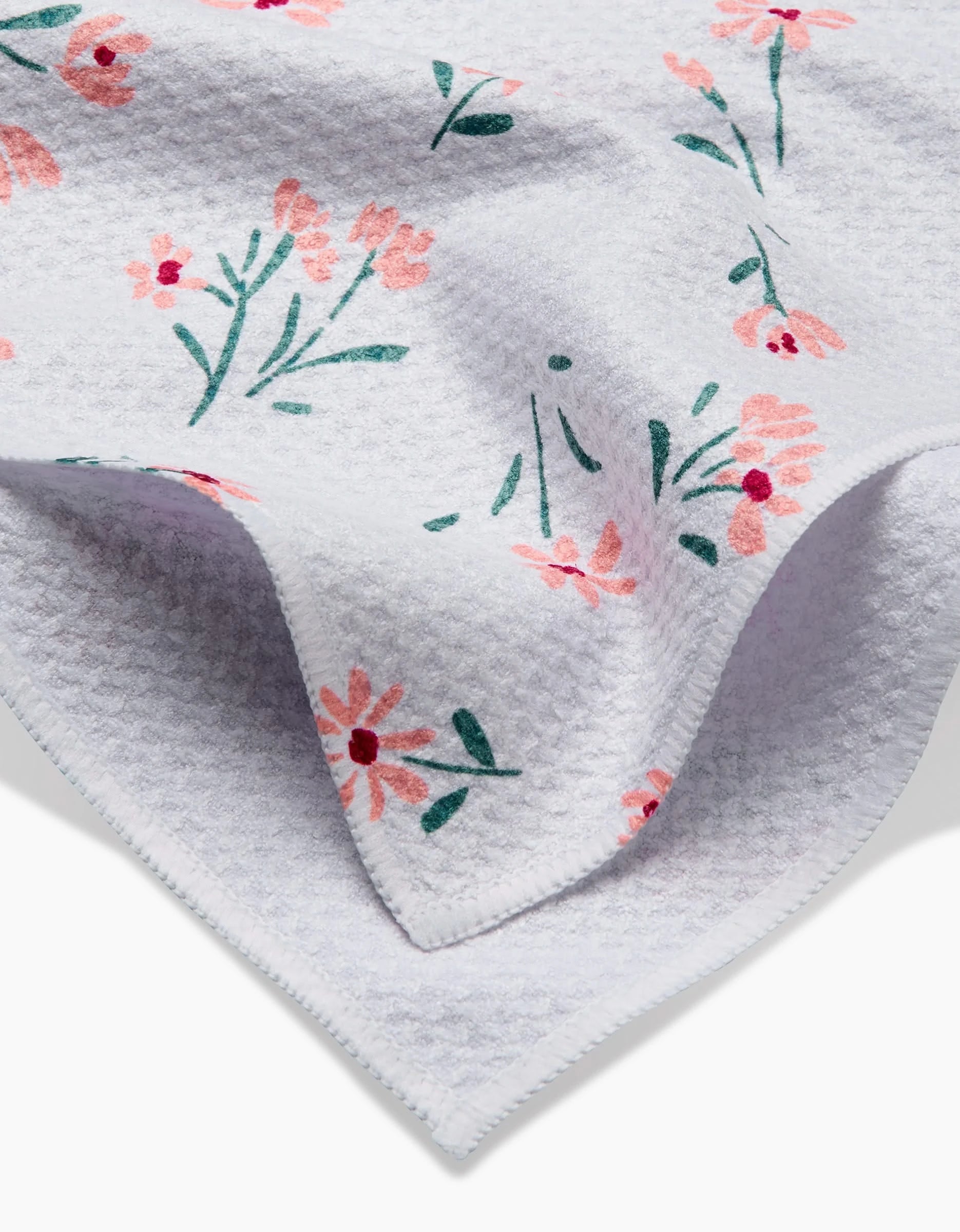 A close-up of Hufton Studios Cottage Garden tea towel, featuring white Geoweave fabric with a subtle waffle pattern and soft texture, adorned with pink and coral floral prints plus green stems and leaves.