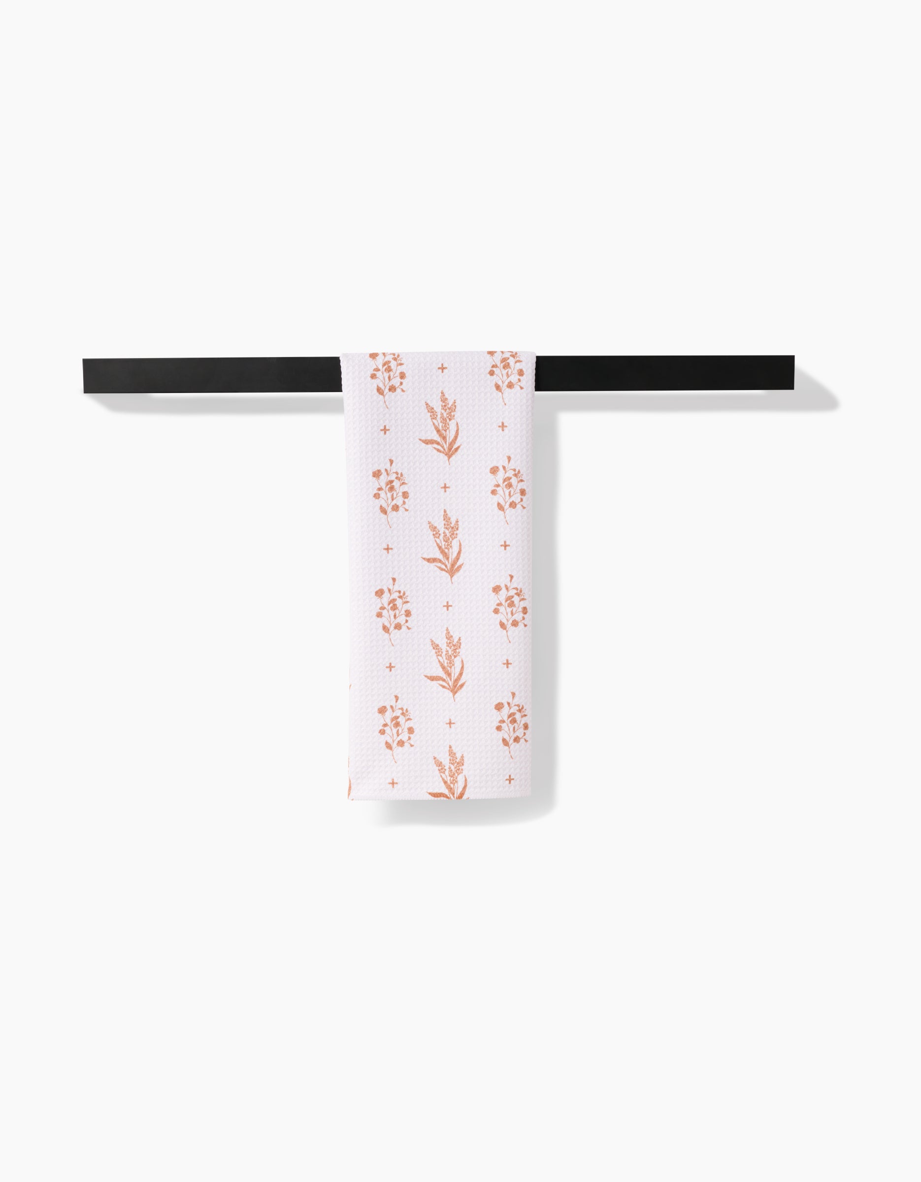 The Country Road tea towel by Charlie Rowan Designs features pinkish-orange floral patterns on white Geoweave fabric, shown neatly folded over a black bar with a plain white background.